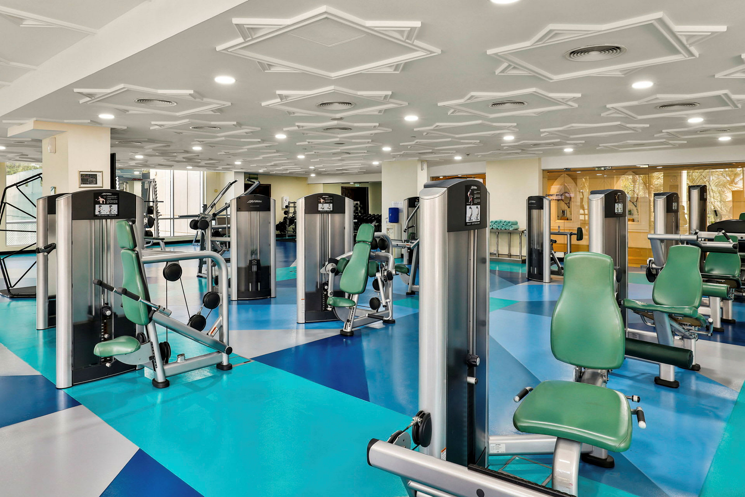 Ett gym med träningsmaskiner och gröna sitsar. (AI-genererad text)