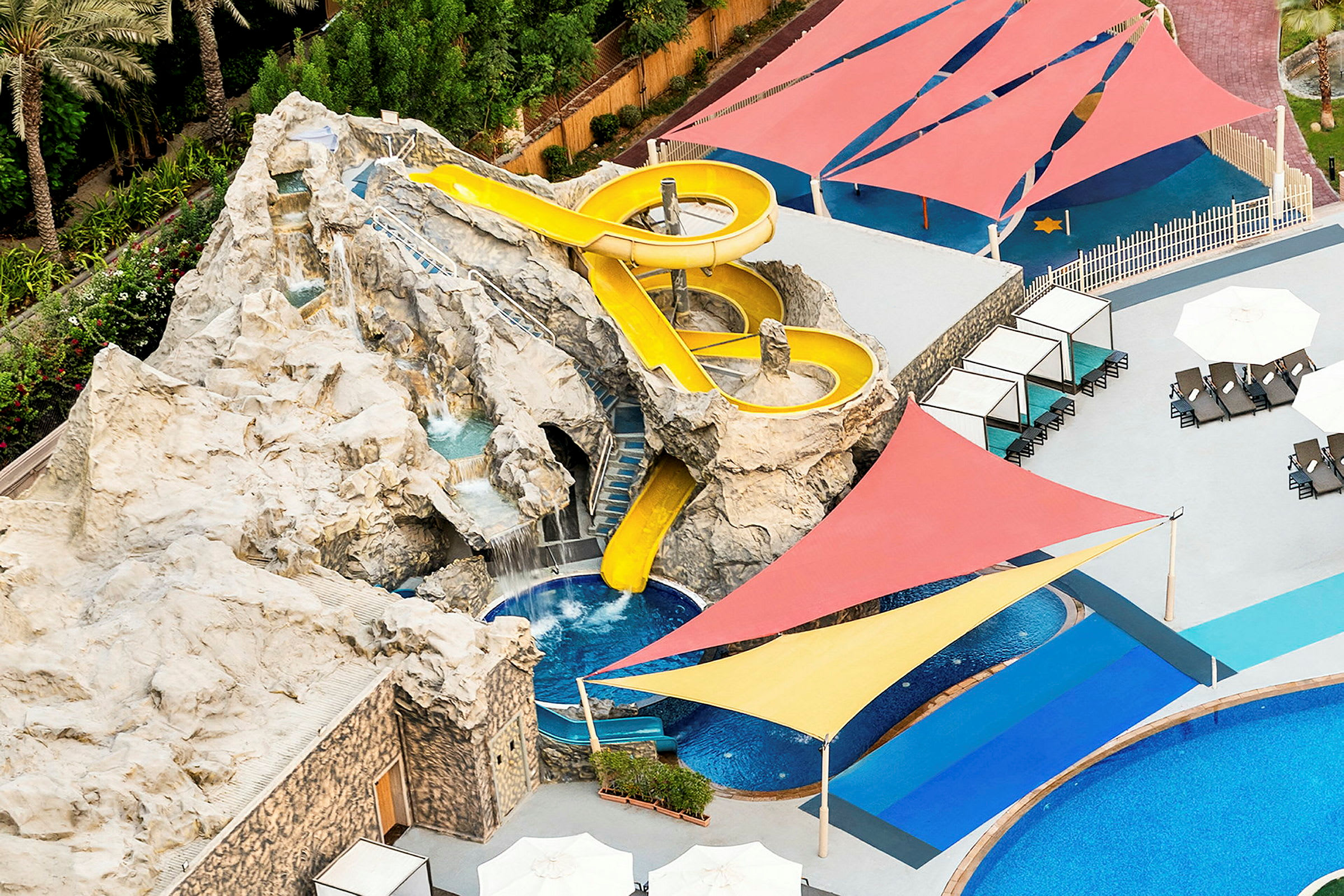 Bild av en vattenrutschkana på en klippformation med tillhörande pool och färgglada solskydd. (AI-genererad text)