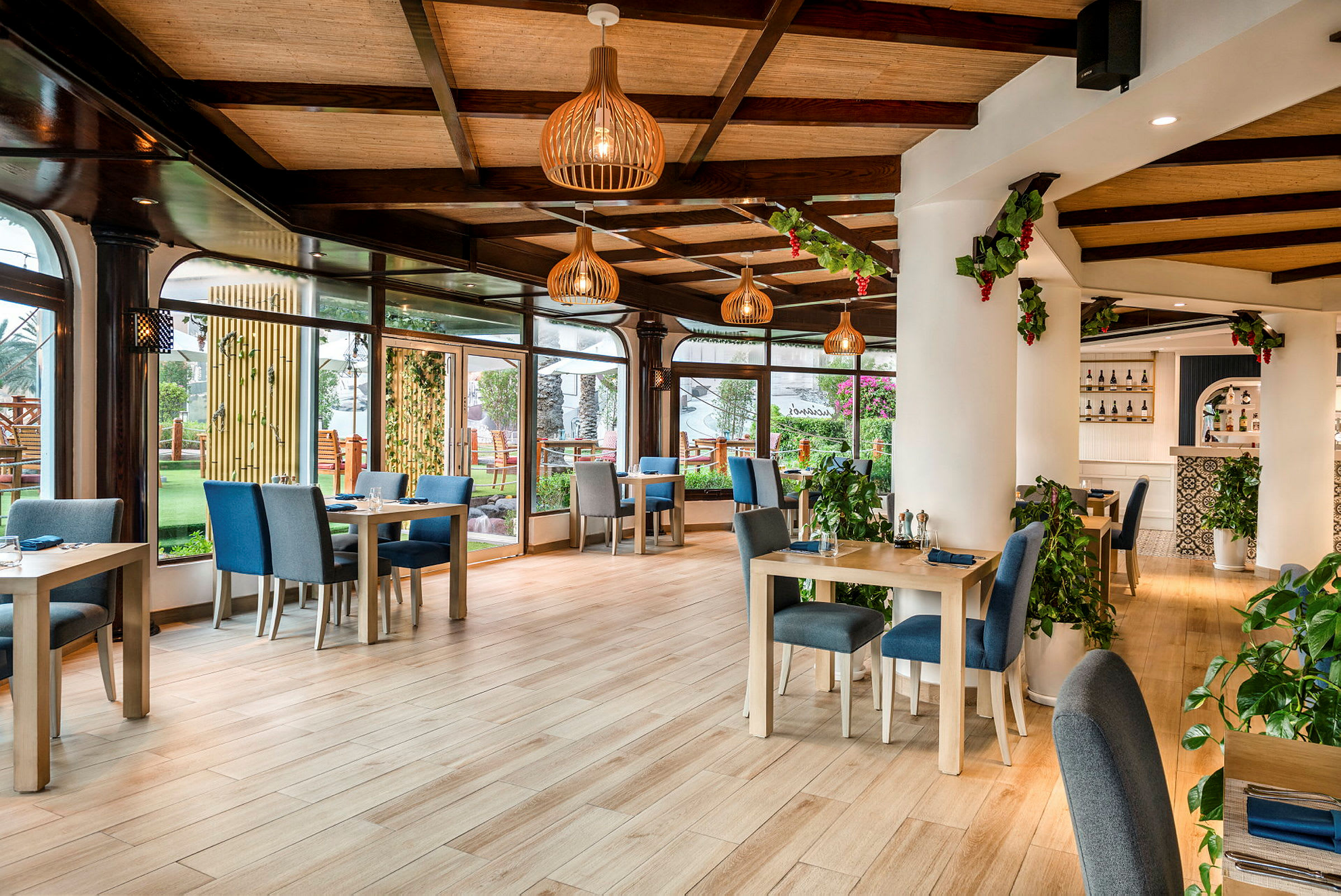 En ljus restaurang med bord och stolar i modernt trädesign, gröna växter och stor fönsteryta med utsikt mot en trädgård. (AI-genererad text)