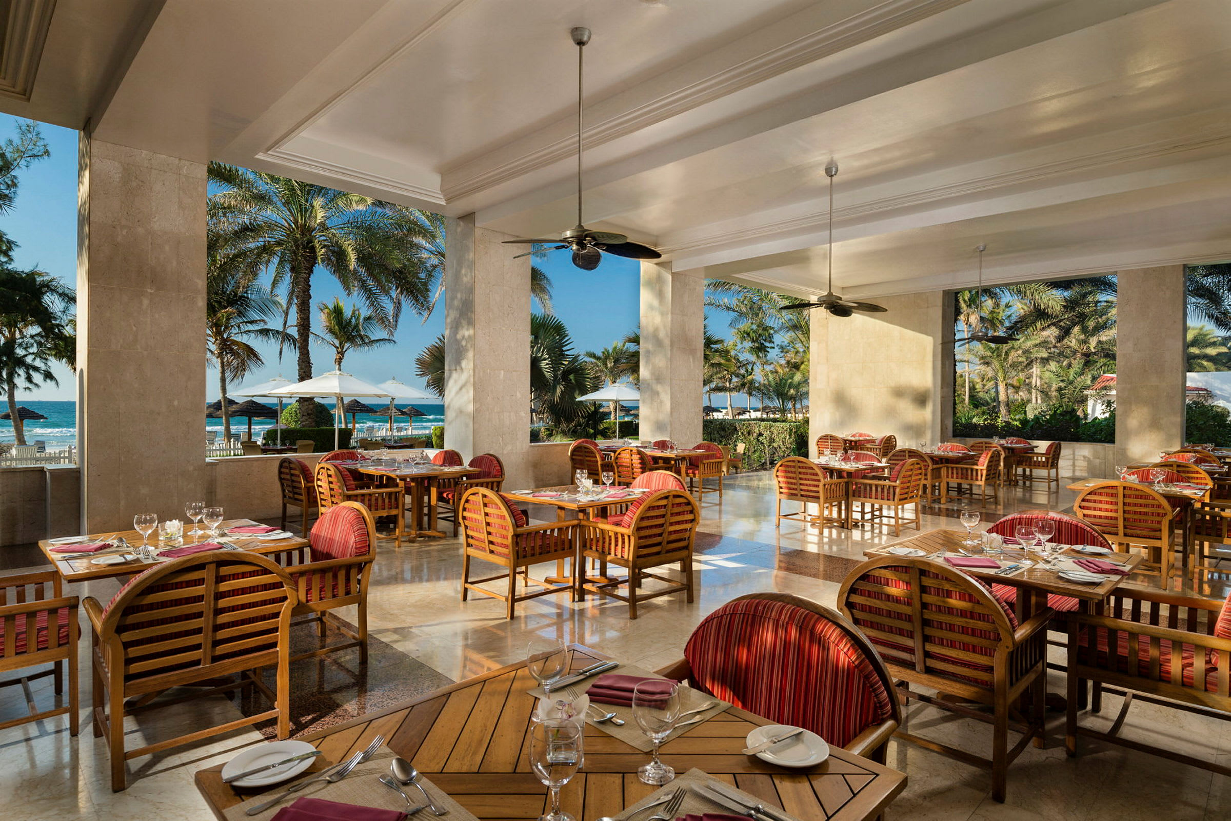 Restaurang med trämöbler och utsikt mot stranden genom stora öppningar. (AI-genererad text)