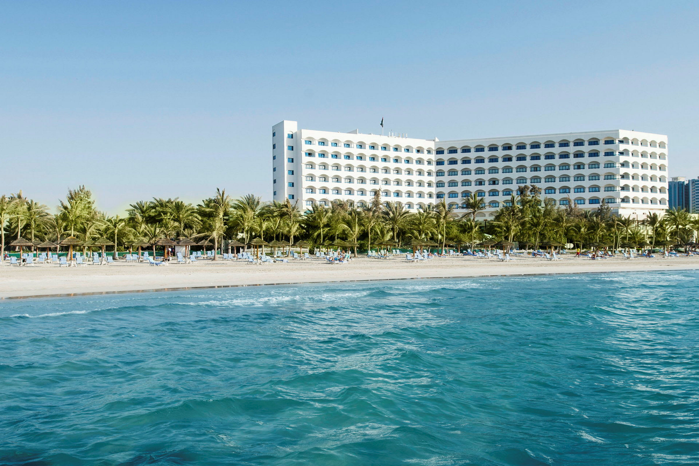 Hotell vid stranden med palmer och solstolar. (AI-genererad text)