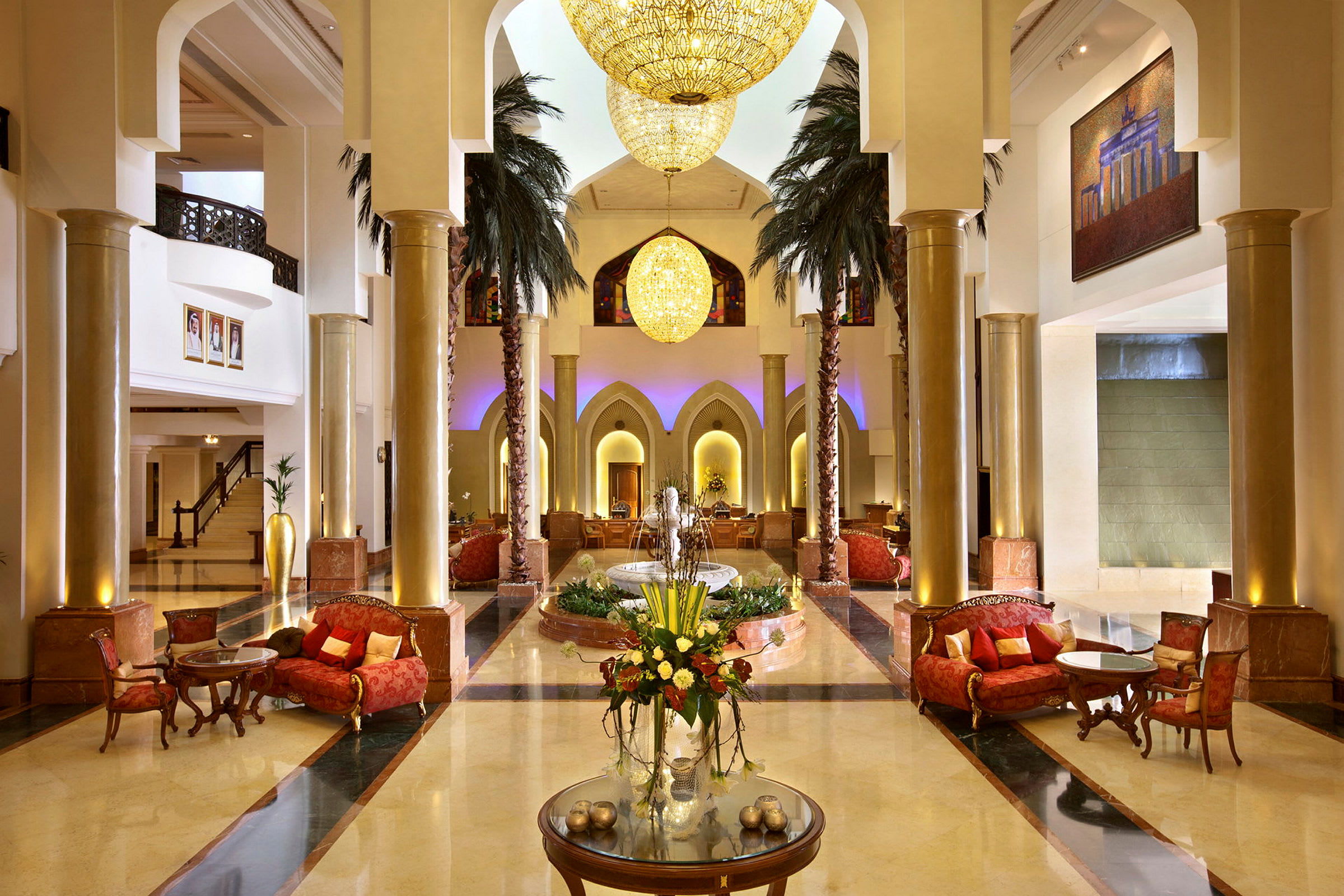 En elegant hotellobby med höga pelare, lysekronor, soffgrupper och en dekorerad fontän i mitten. (AI-genererad text)