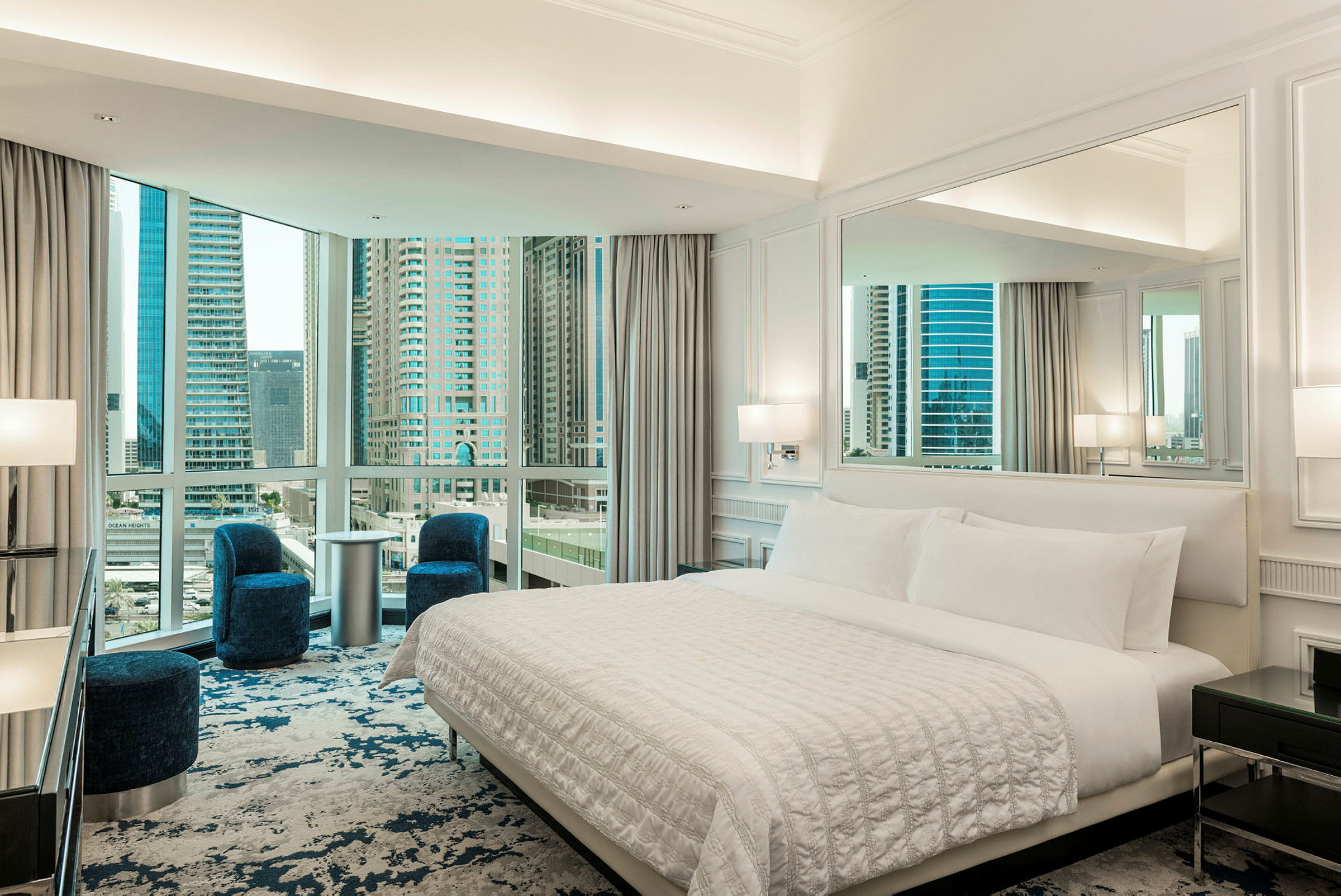 Ett hotellrum med en stor säng och sittmöbler, samt stora fönster med utsikt över stadens skyline. (AI-genererad text)