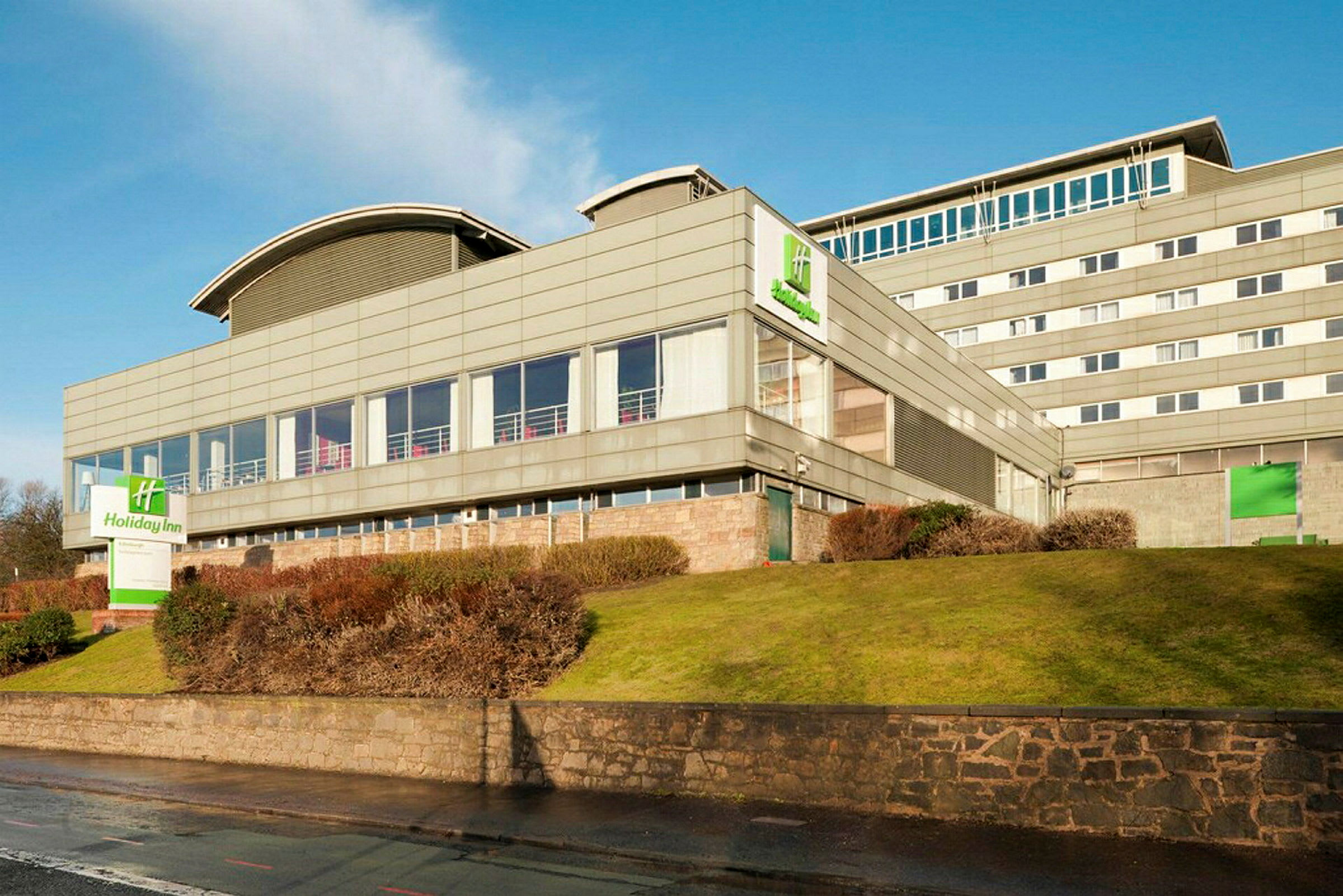 Holiday Inn-hotell i en modern byggnad med omgivande gräsmatta och buskar. (AI-genererad text)