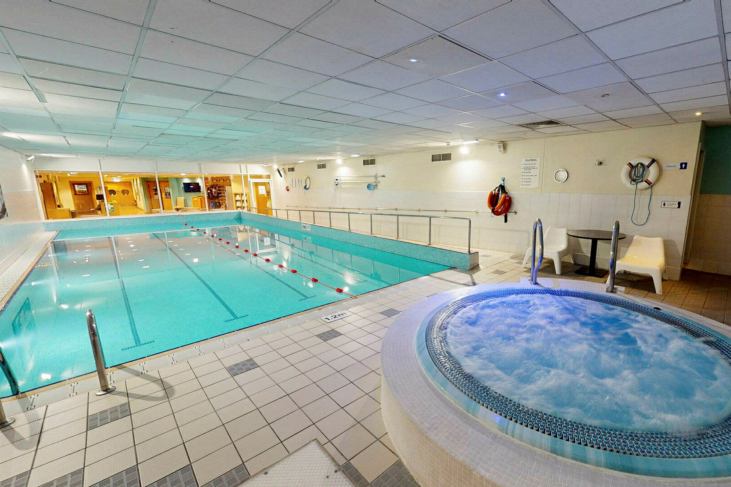 Inomhuspoolområde med en stor pool och en bubbelpool. (AI-genererad text)