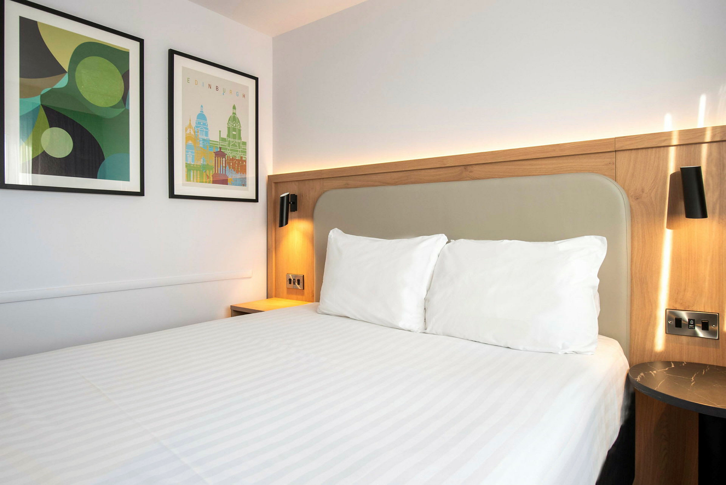 En hotellrumssäng med vita sängkläder och två tavlor på väggen. (AI-genererad text)
