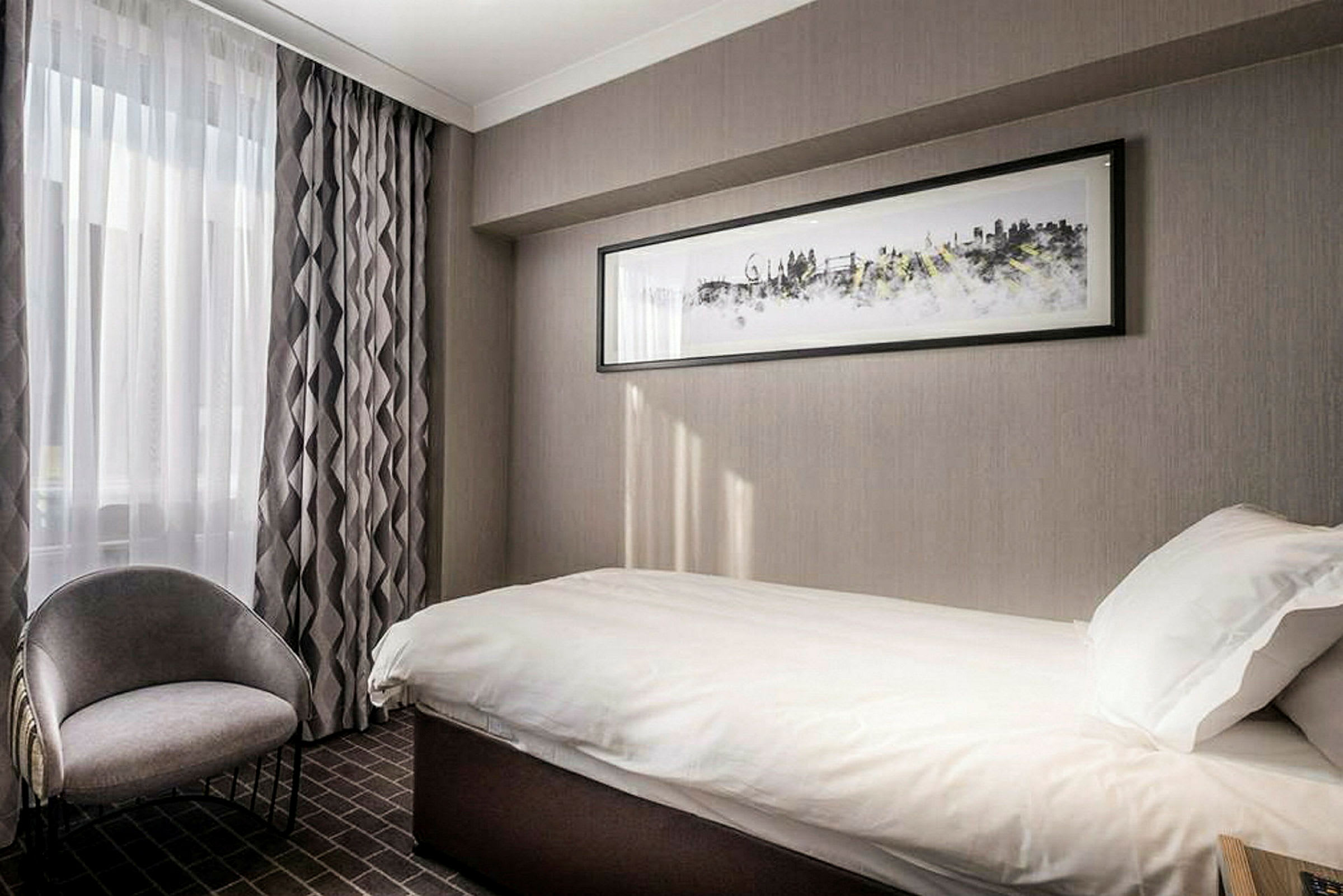 Hotellrum med enkelsäng och stol, dekorerat med gråa färger. (AI-genererad text)