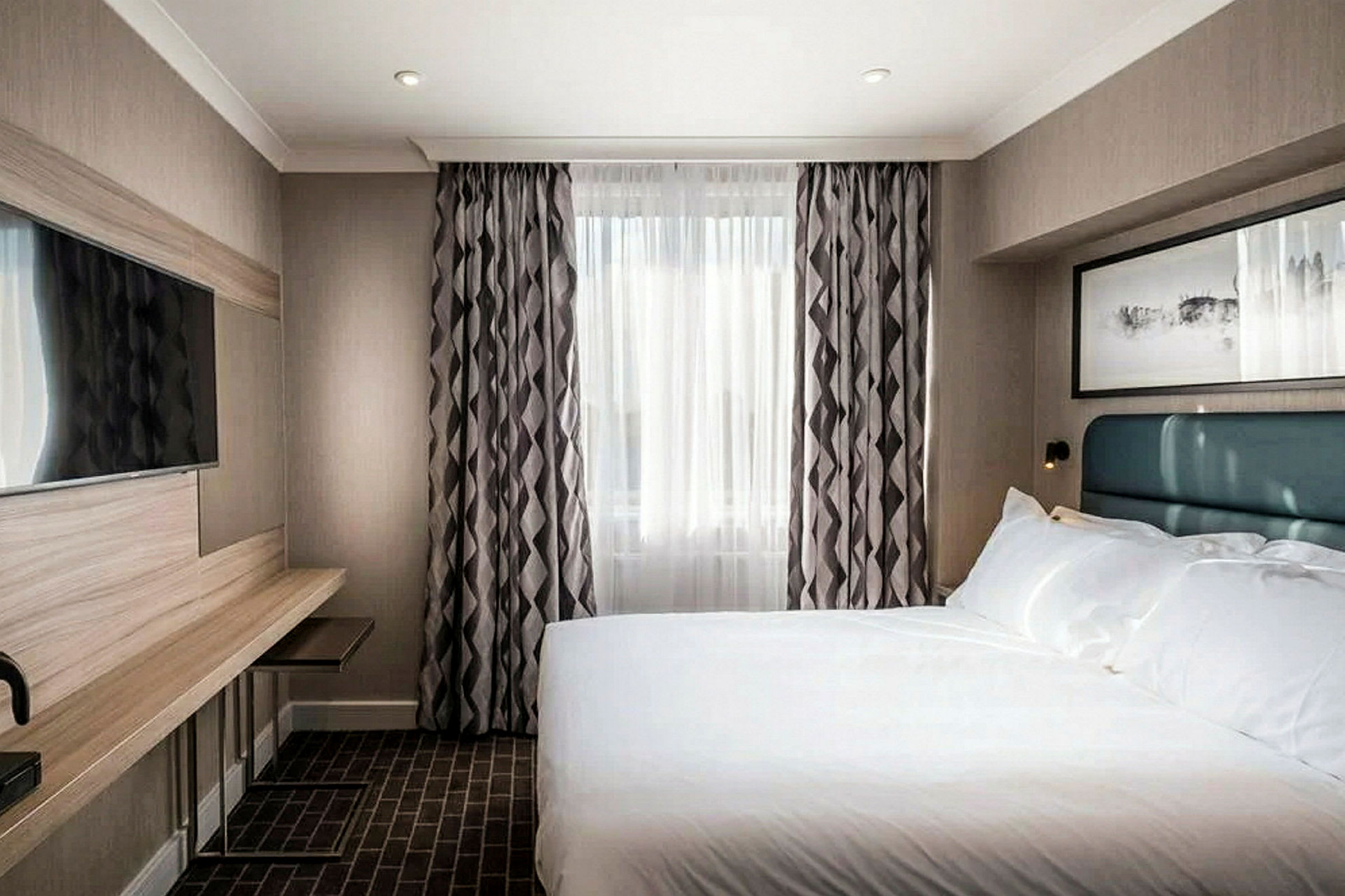 Bild av ett hotellrum med en säng, TV och ett fönster med gardiner. (AI-genererad text)