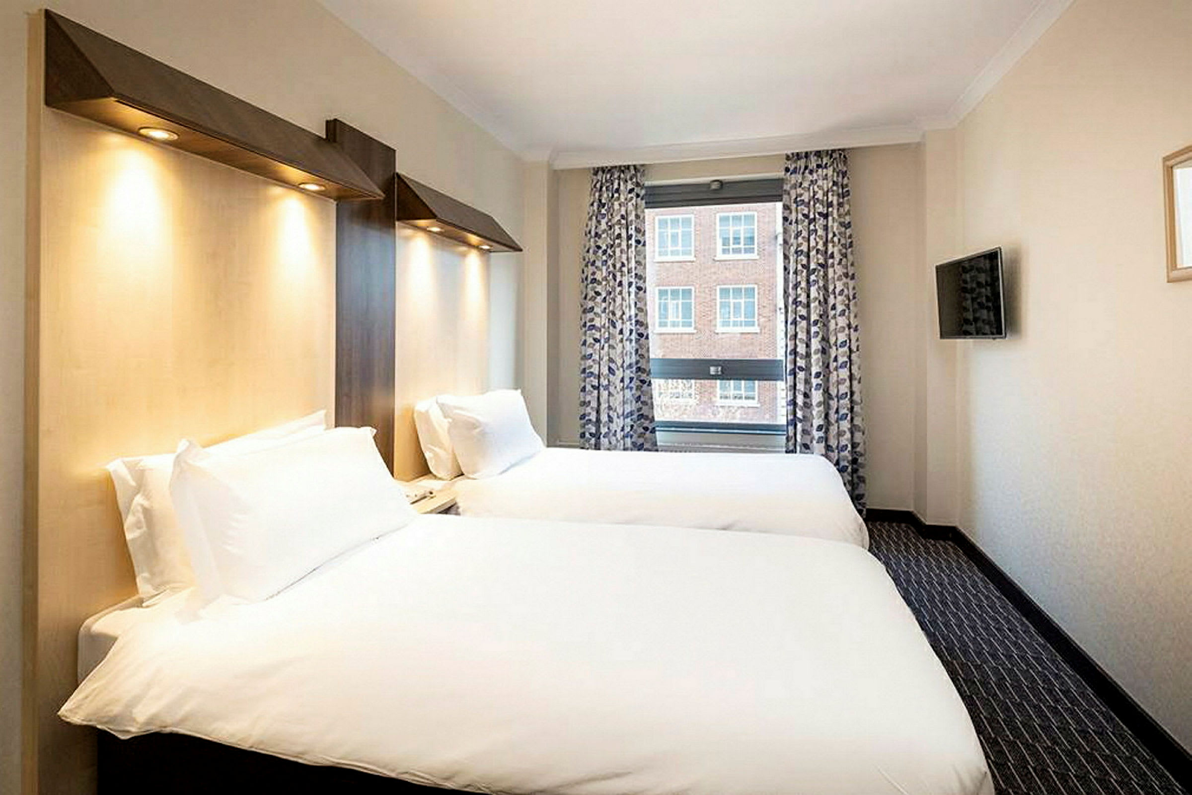 Ett hotellrum med två enkelsängar, ett fönster med utsikt och en väggmonterad TV. (AI-genererad text)