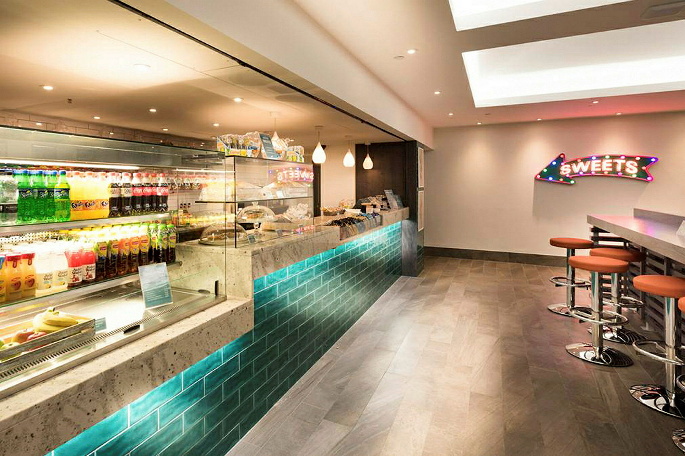 Bild av en modern caféinteriör med en glasmonter fylld med drycker och snacks samt sittplatser vid en disk. (AI-genererad text)