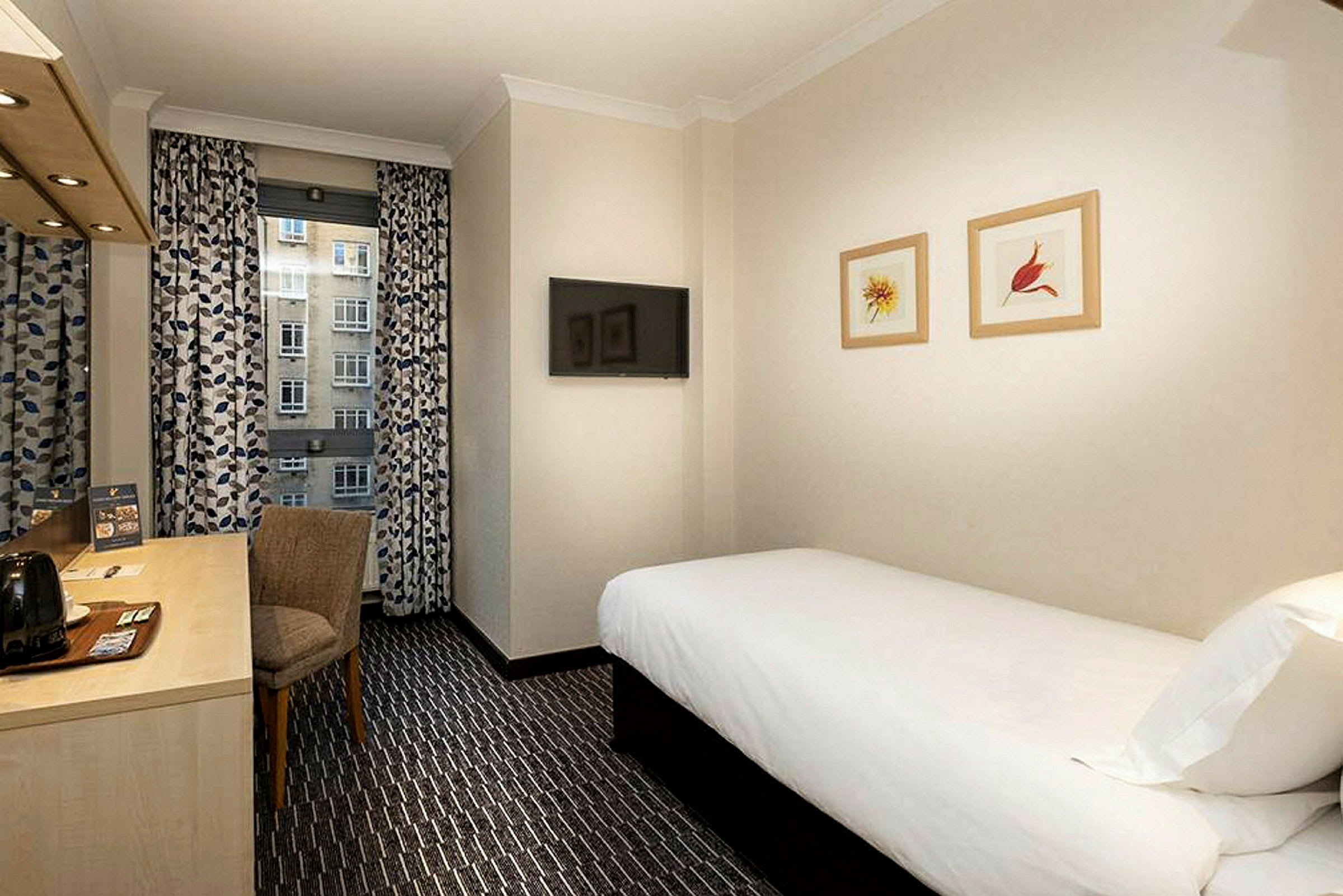 Bild på ett hotellrum med en enkelsäng, ett skrivbord med stol och en TV på väggen. (AI-genererad text)