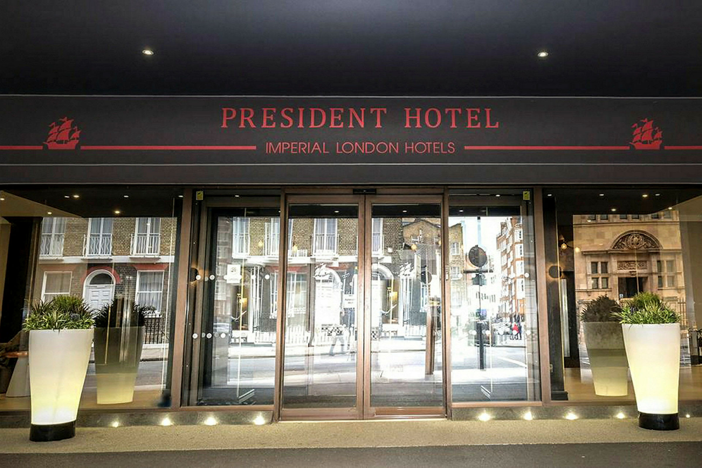 Huvudentrén till President Hotel med glasdörrar och blomkrukor. (AI-genererad text)