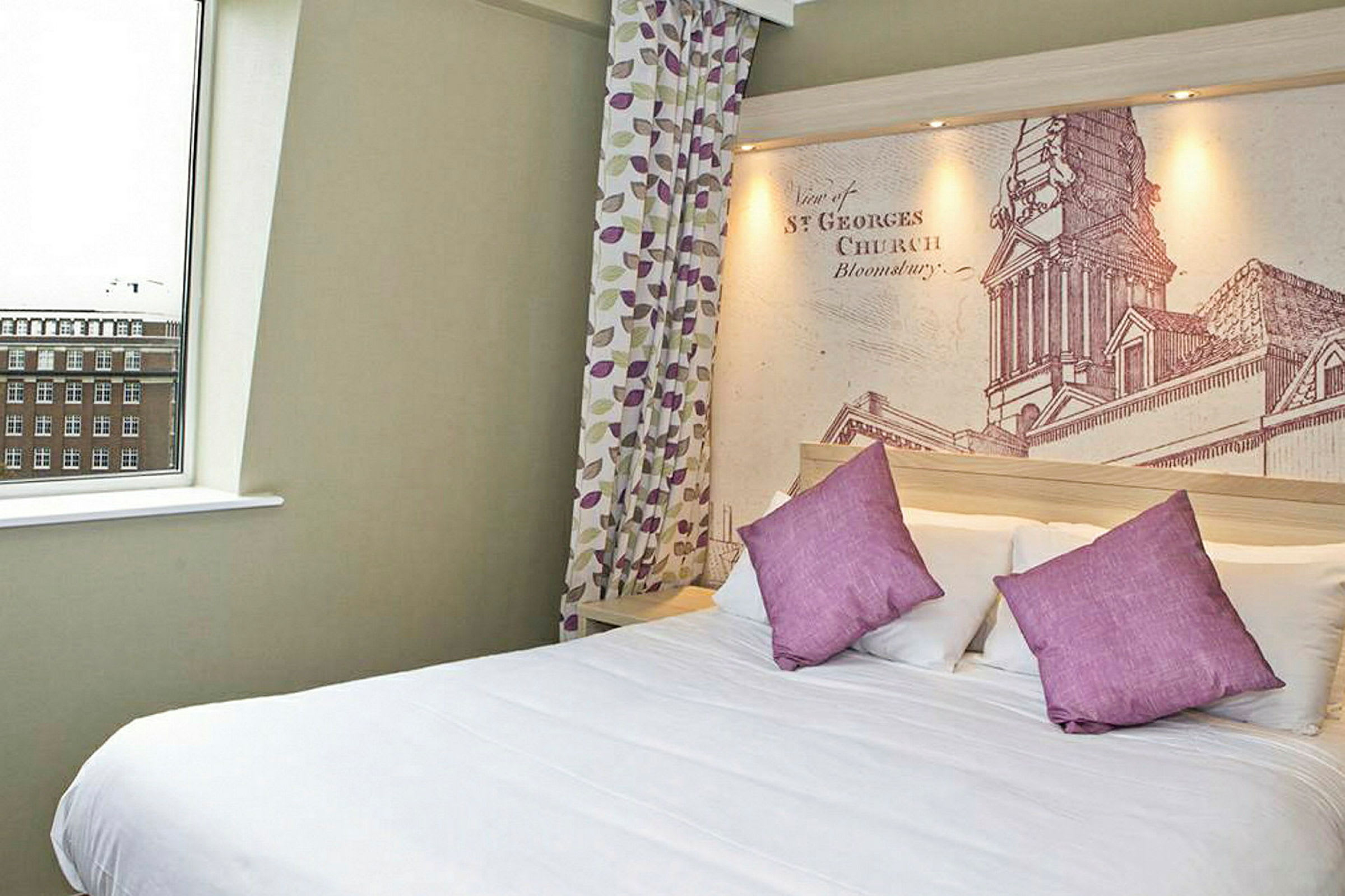 Hotellets sovrum med en stor säng, lila kuddar och detaljerad väggmålning bakom sängen. (AI-genererad text)