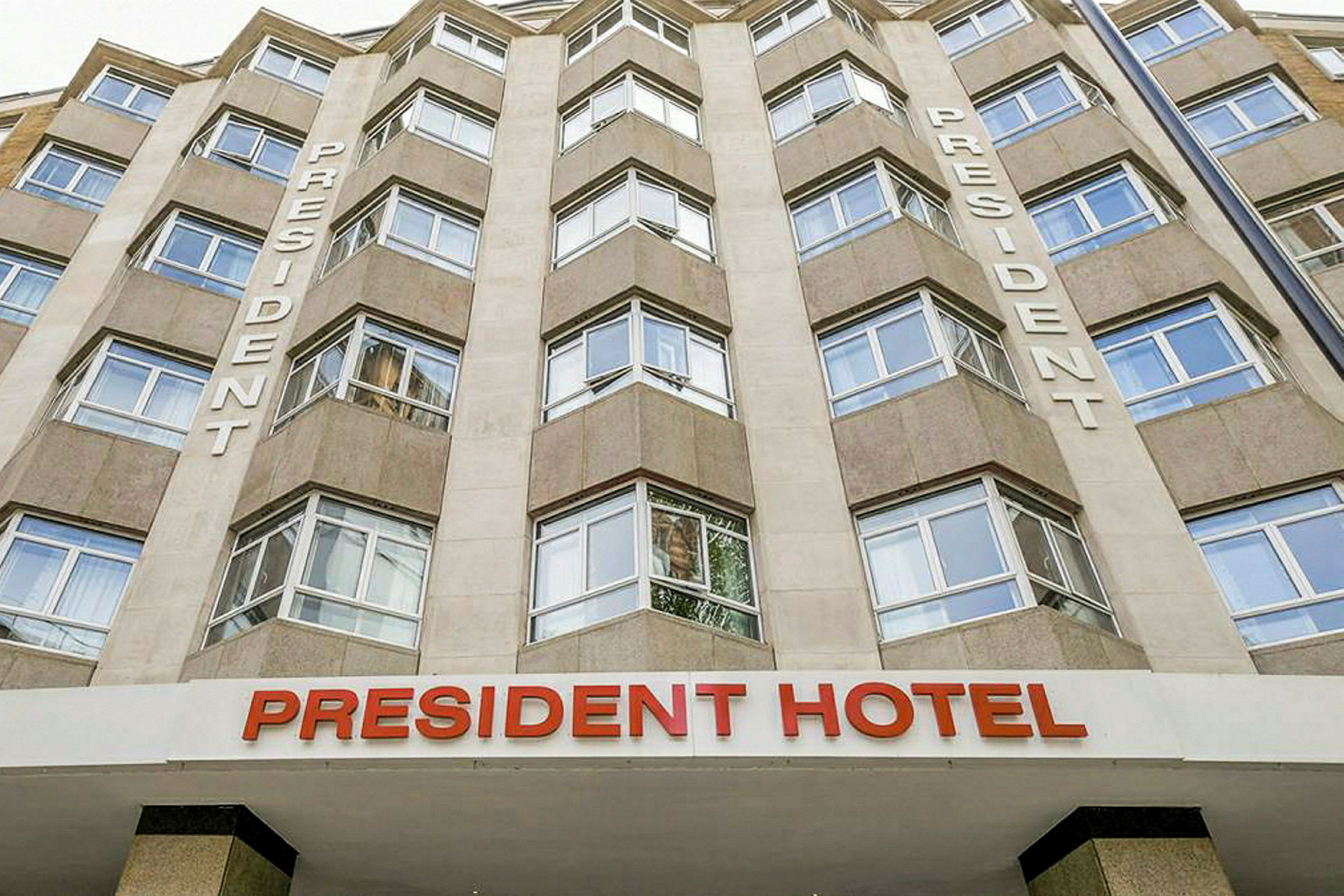 Klassisk fasad av President Hotel med stora fönster och texten 'President' på väggen. (AI-genererad text)