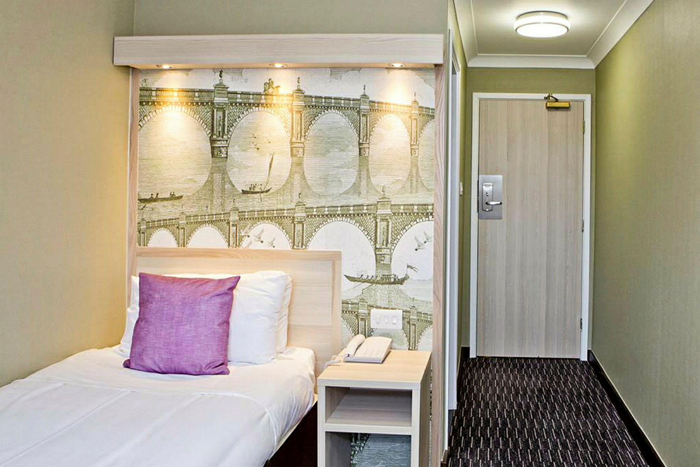 Ett hotellrum med en enkelsäng och en väggmålning med bromotiv. (AI-genererad text)