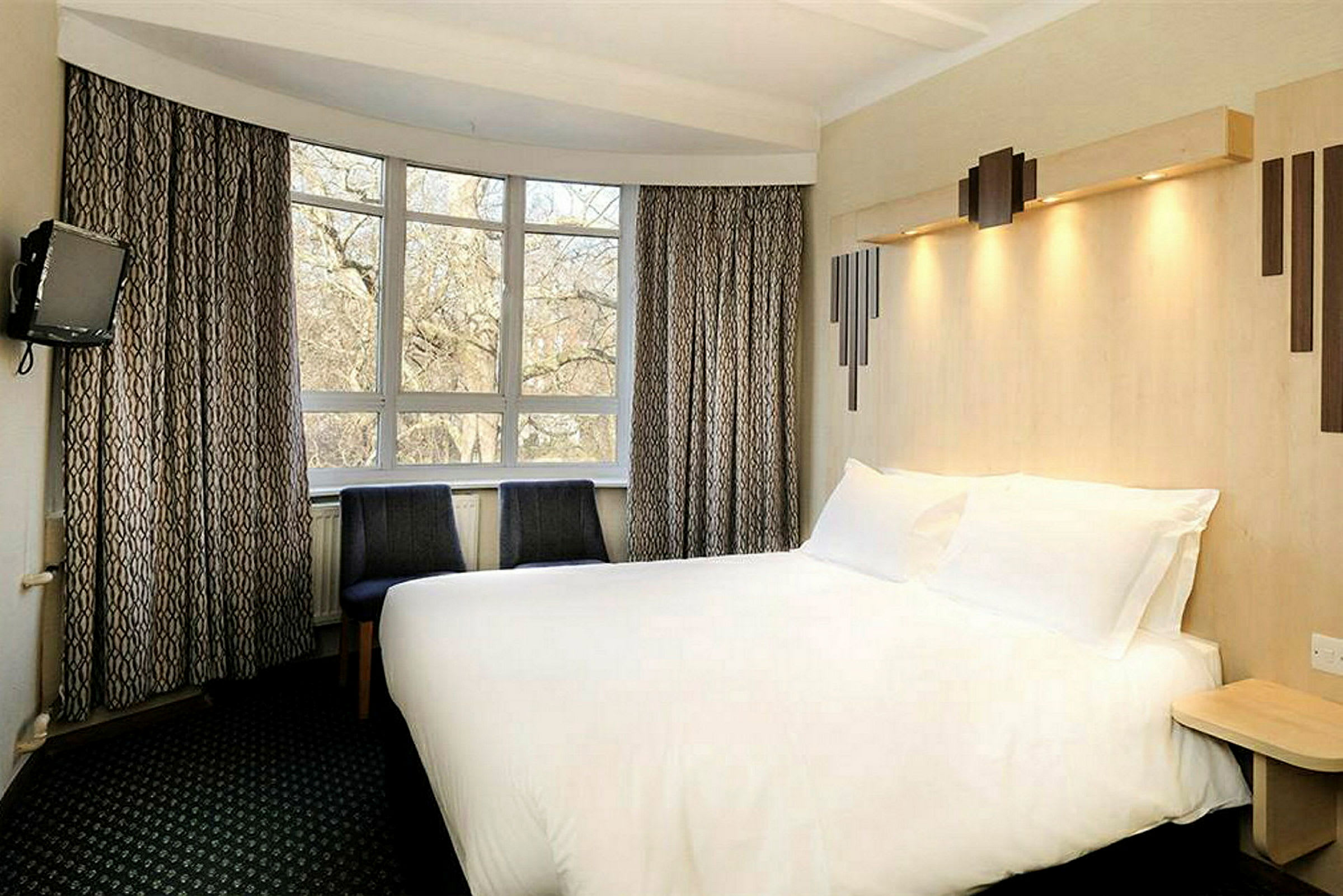 Ett hotellrum med en stor säng, två stolar och ett fönster med trädutsikt. (AI-genererad text)