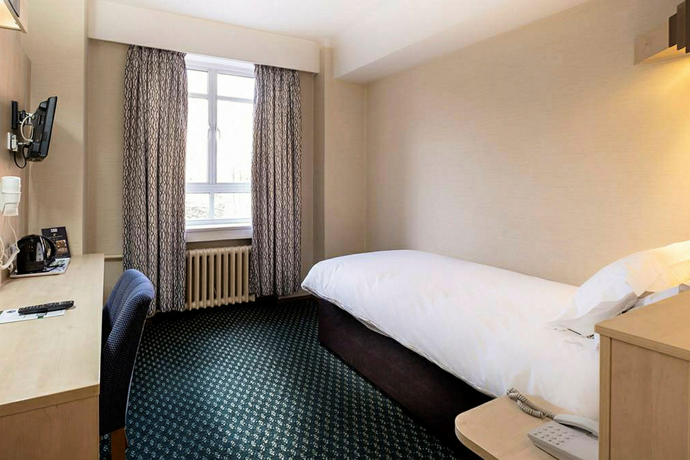 Ett hotellrum med en enkelsäng och skrivbord vid fönstret. (AI-genererad text)