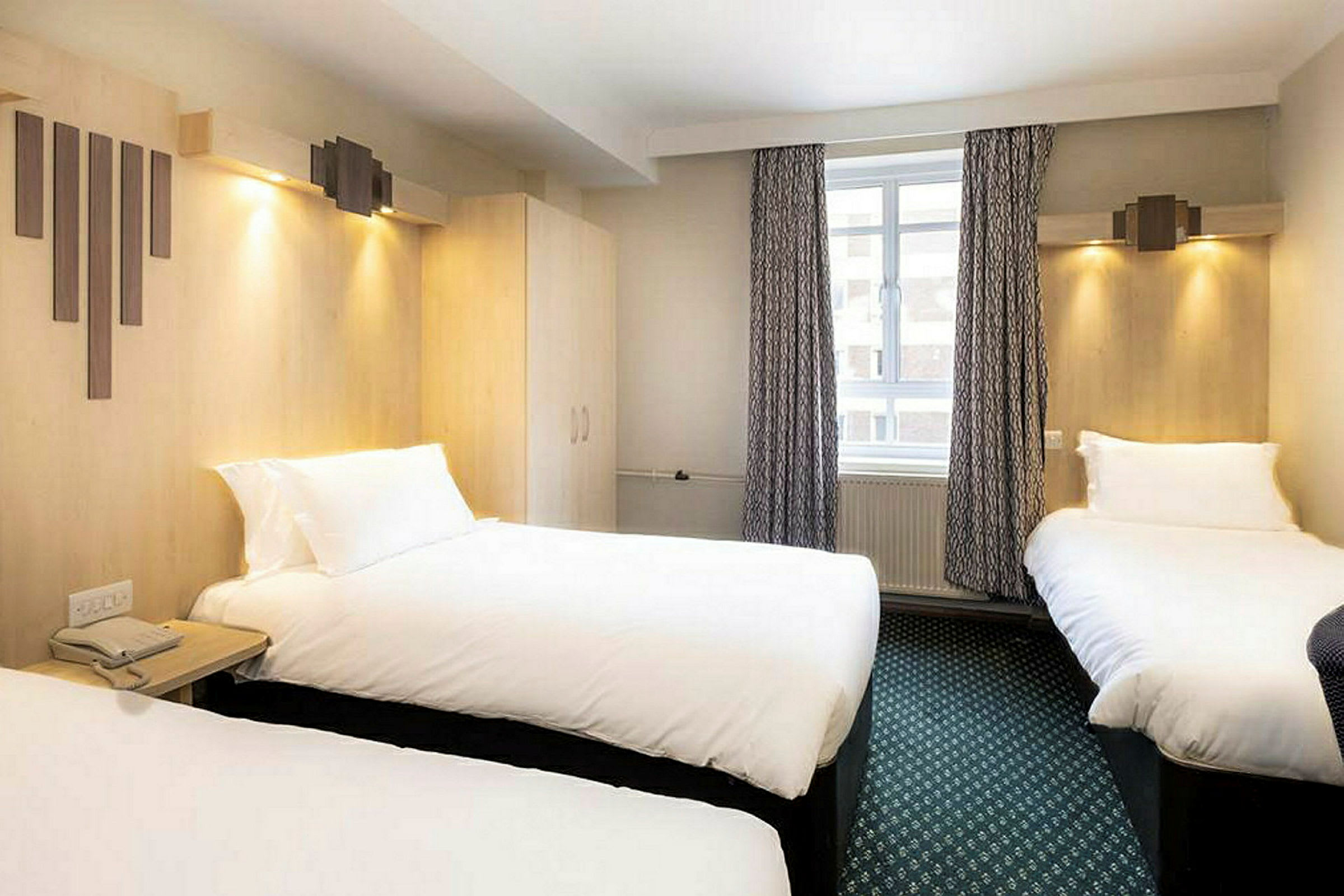 Ett hotellrum med tre bäddar, gardiner och ett fönster. (AI-genererad text)