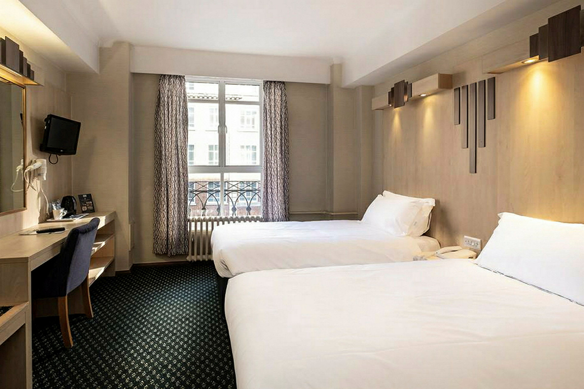 Ett hotellrum med två enkelsängar, en arbetsyta med stol och ett fönster som släpper in naturligt ljus. (AI-genererad text)