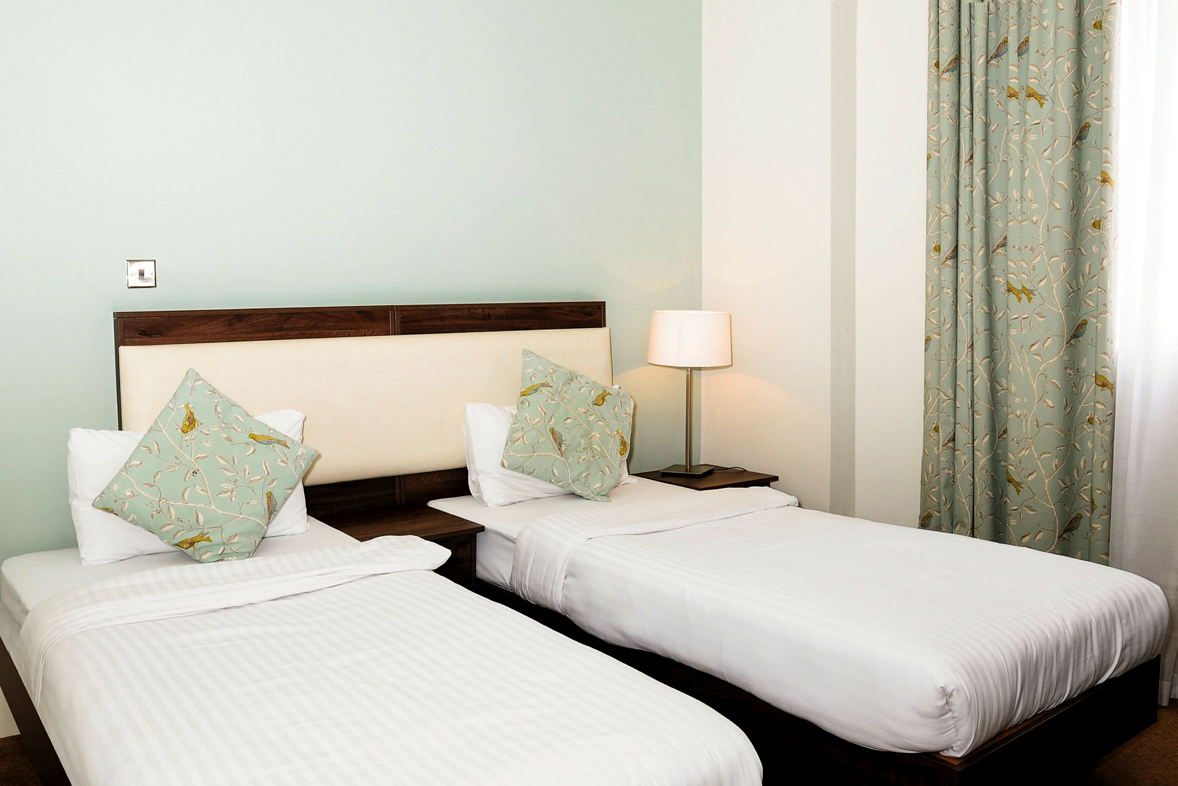 Hotellrum med två enkelsängar, prydnadskuddar och lampa. (AI-genererad text)