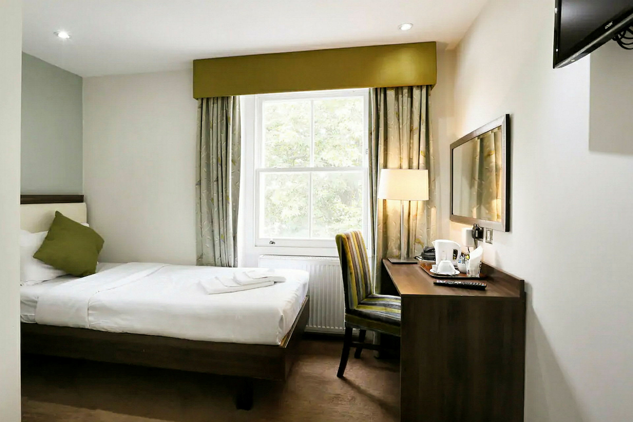 Hotellrum med en enkelsäng, fönster, skrivbord och stol. (AI-genererad text)