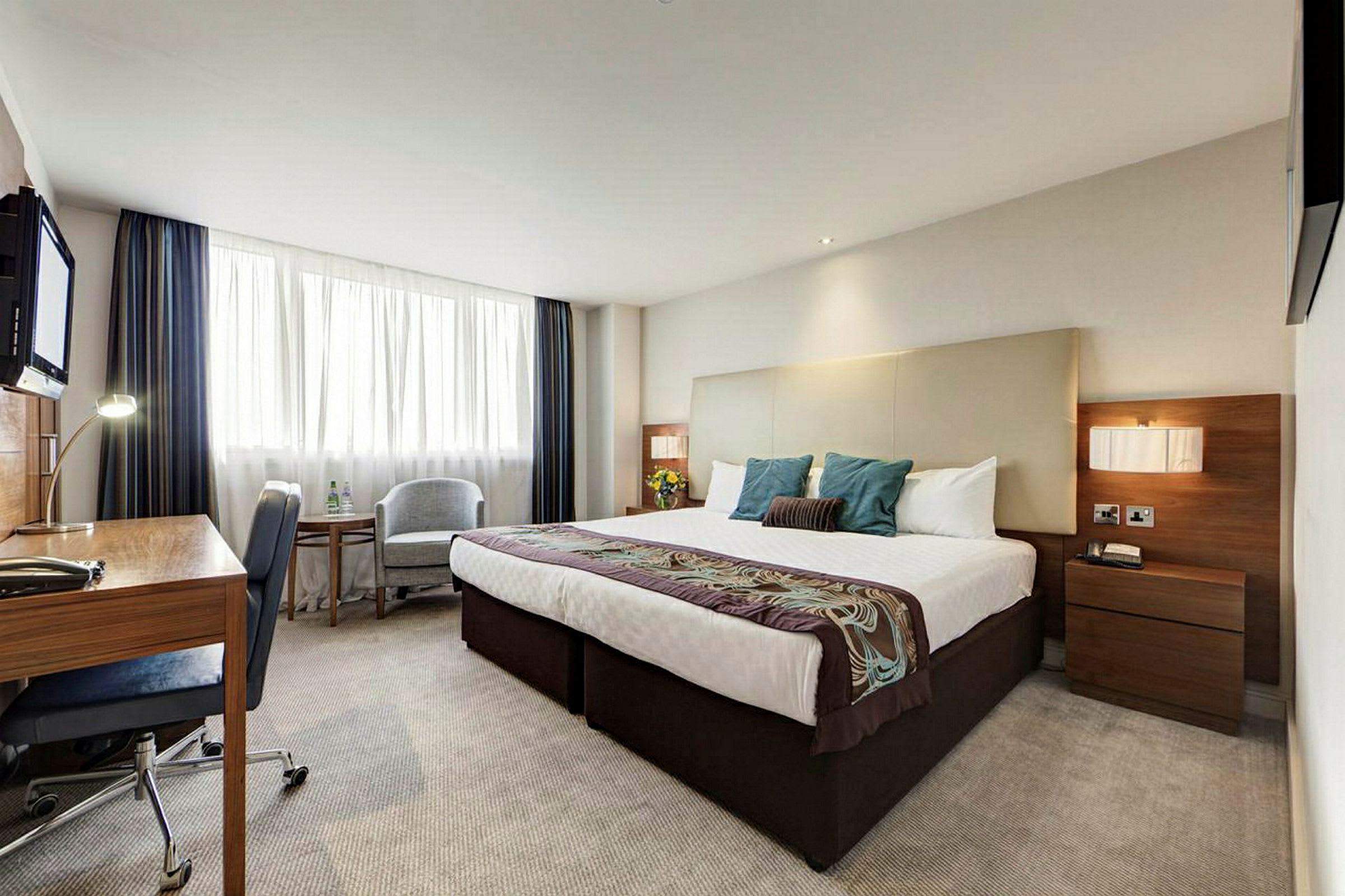 Hotellrum med dubbelsäng, skrivbord och stol. (AI-genererad text)