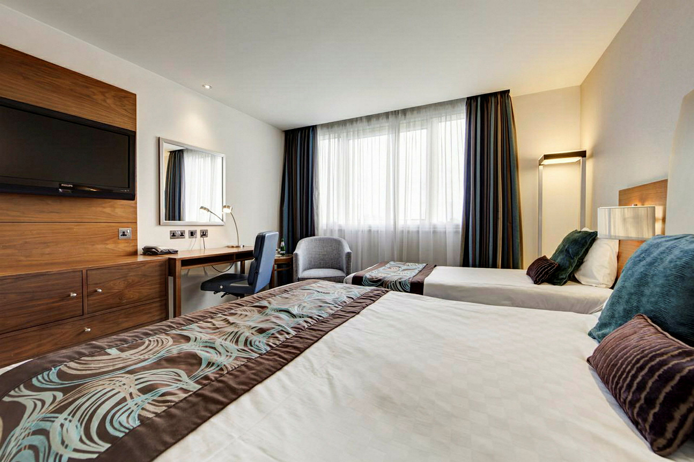 Ett hotellrum med två enkelsängar, ett skrivbord och en tv på väggen. (AI-genererad text)