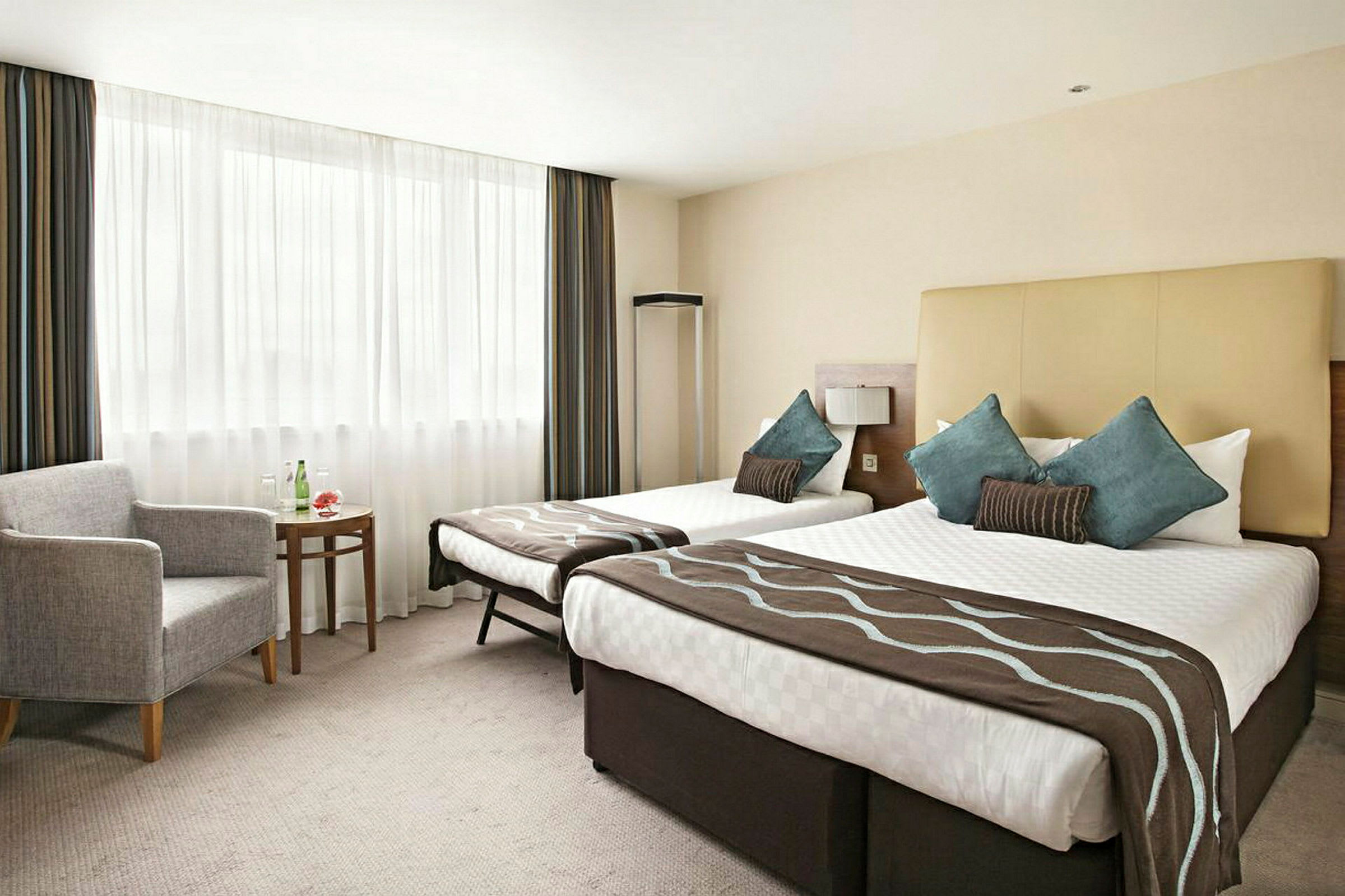 Hotellrum med två breda sängar, sittgrupp och fönster med ljusa gardiner. (AI-genererad text)