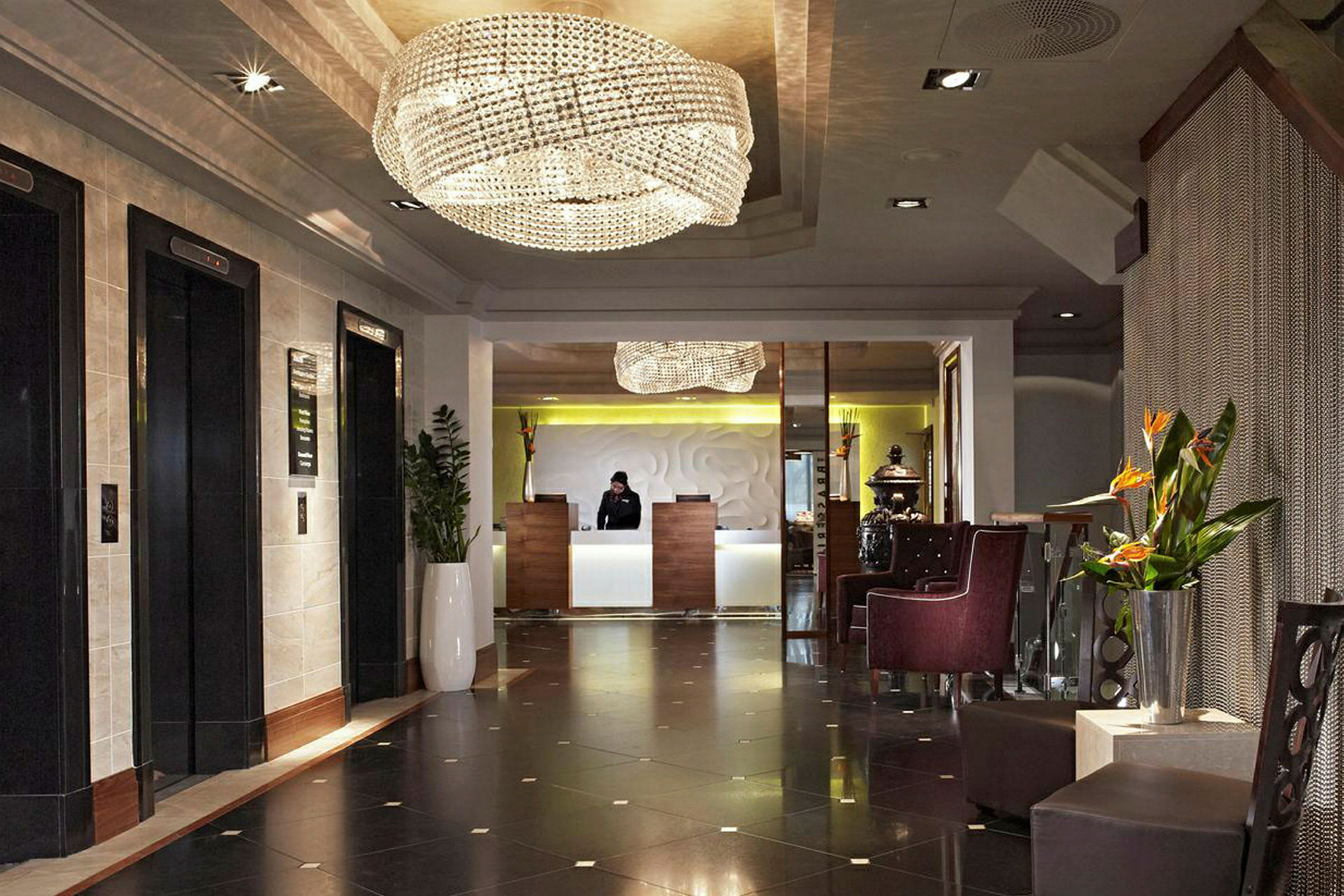 Hotellfoajé med reception och vänteområde, dekorerad med ljuskrona och växter. (AI-genererad text)