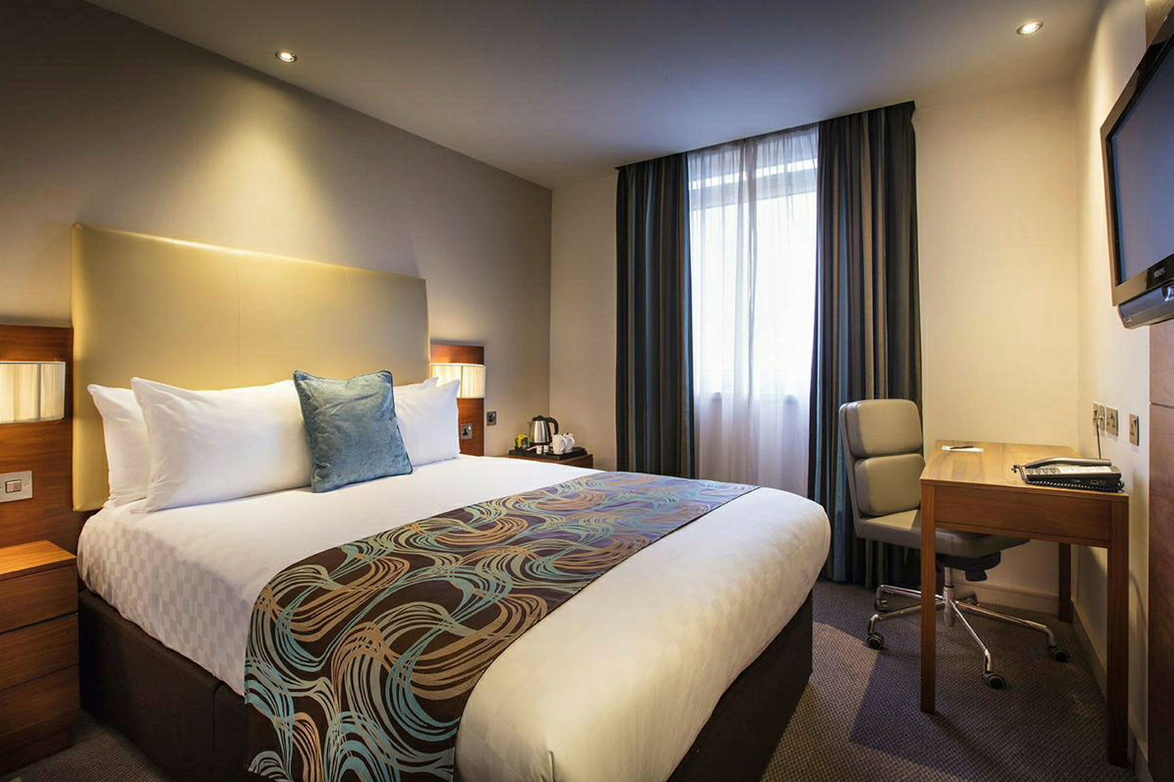 Hotellrum med en stor säng, skrivbord och stol. (AI-genererad text)
