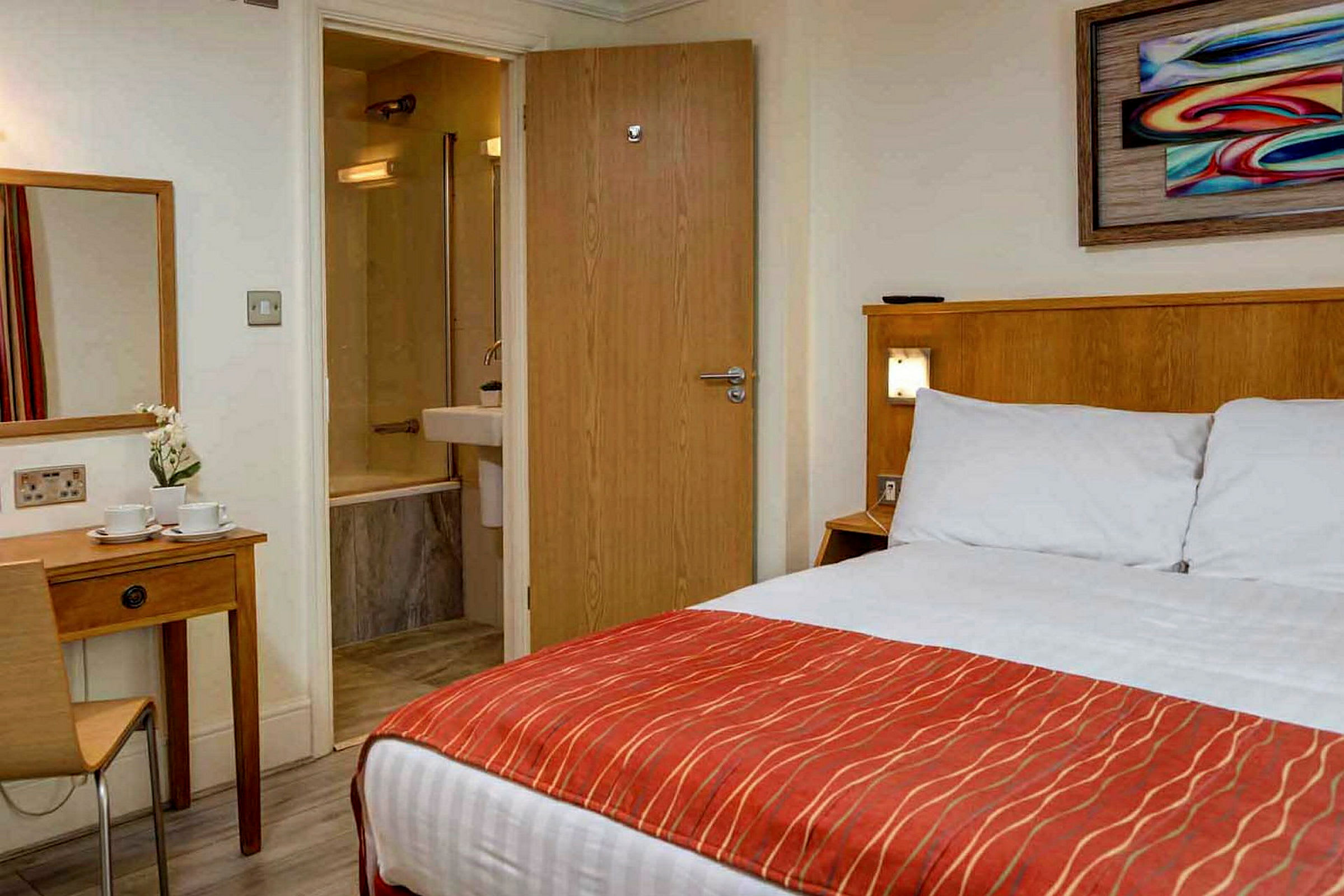 Ett hotellrum med en säng, ett skrivbord och en dörr som leder till ett badrum. (AI-genererad text)