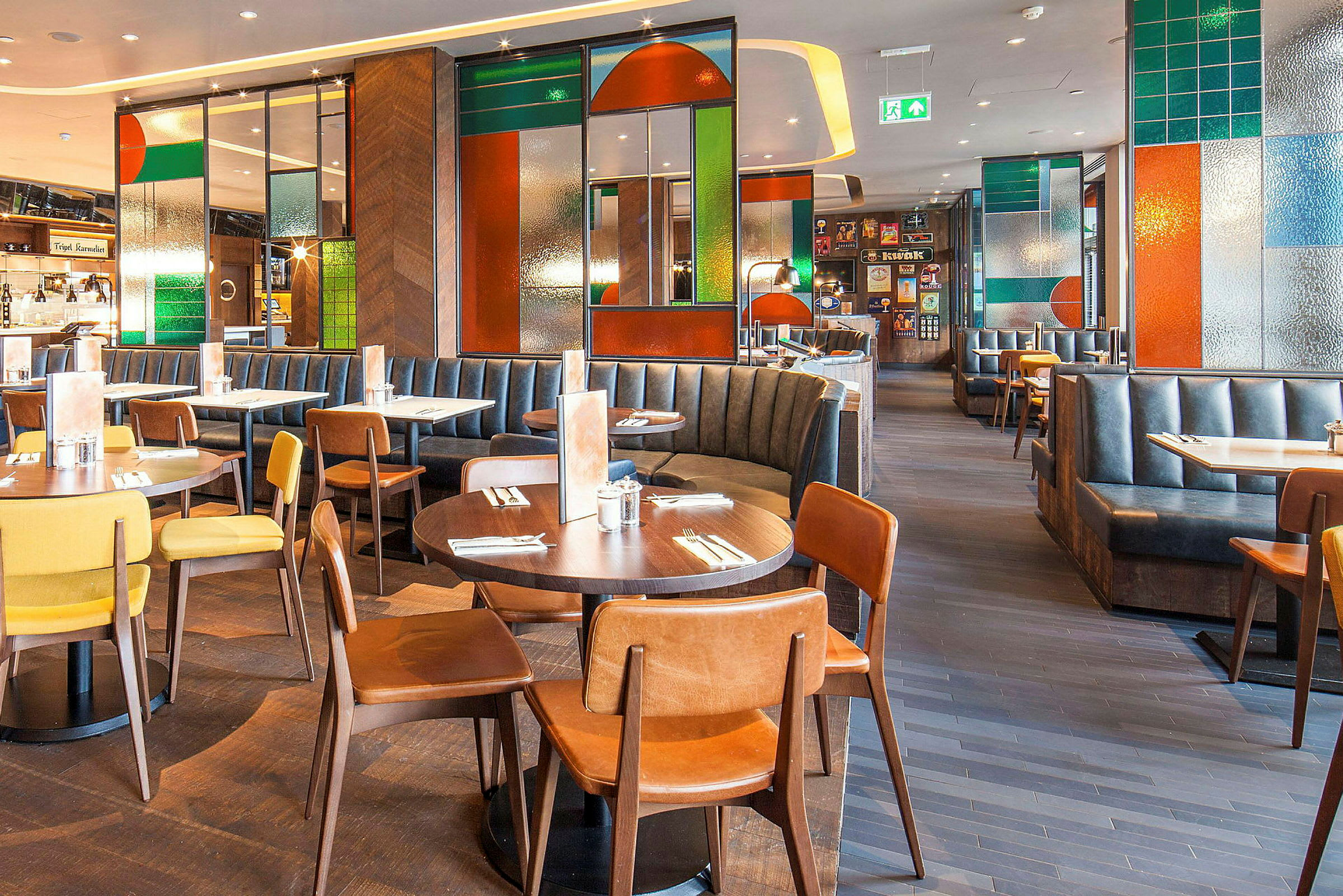 En restaurang med bord, stolar och bås, inredd med färgade glasdetaljer. (AI-genererad text)