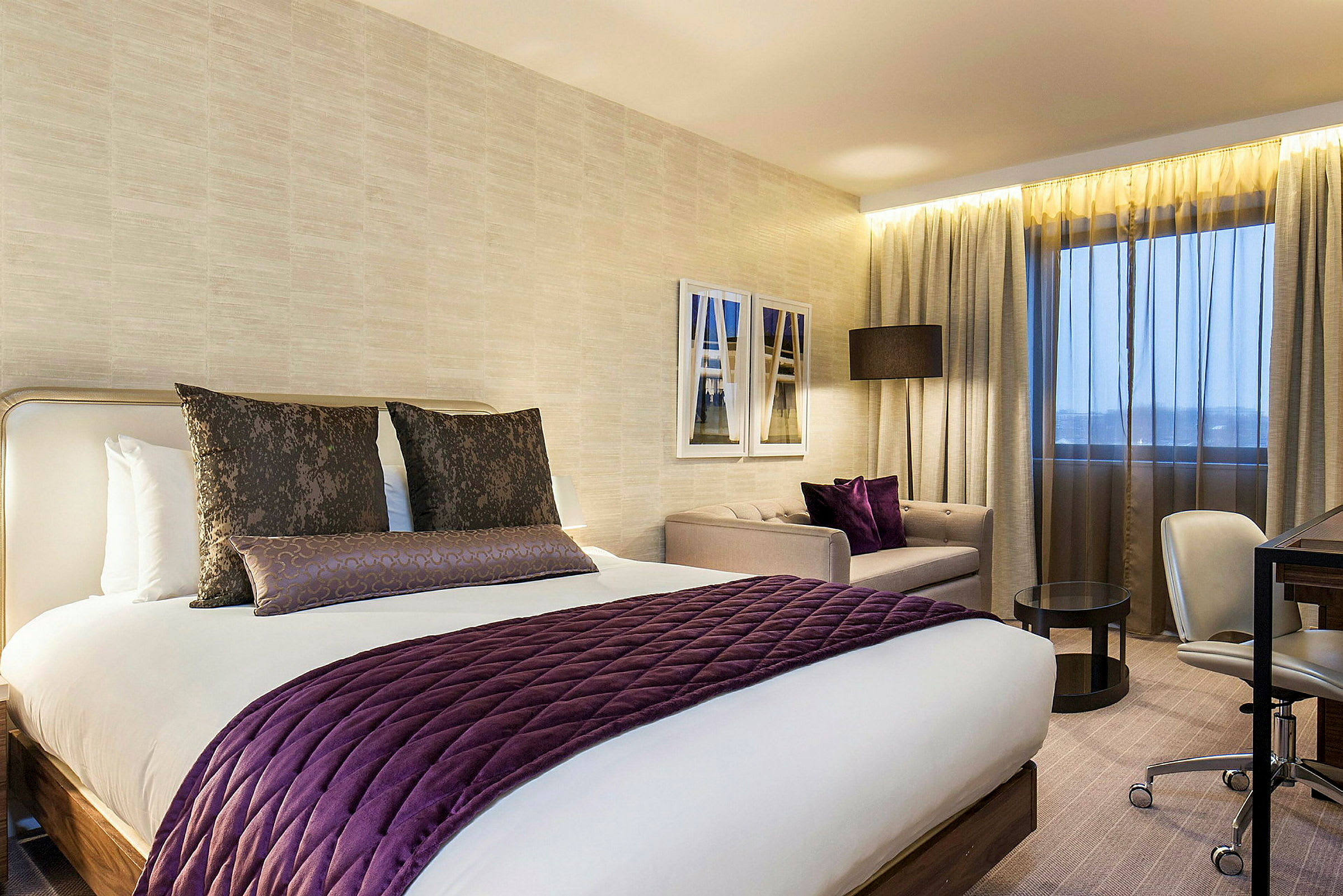 Ett hotellrum med modern inredning, inklusive en stor säng med lila detaljer, en sittgrupp och skrivbord. (AI-genererad text)