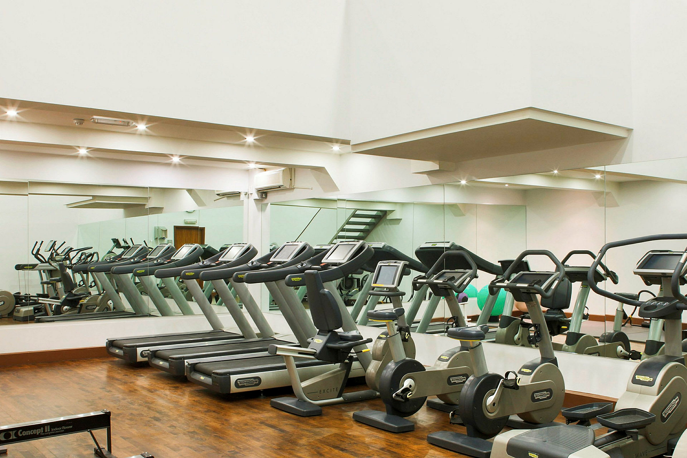 Ett gym med träningsmaskiner inklusive löpband och motionscyklar framför speglar. (AI-genererad text)