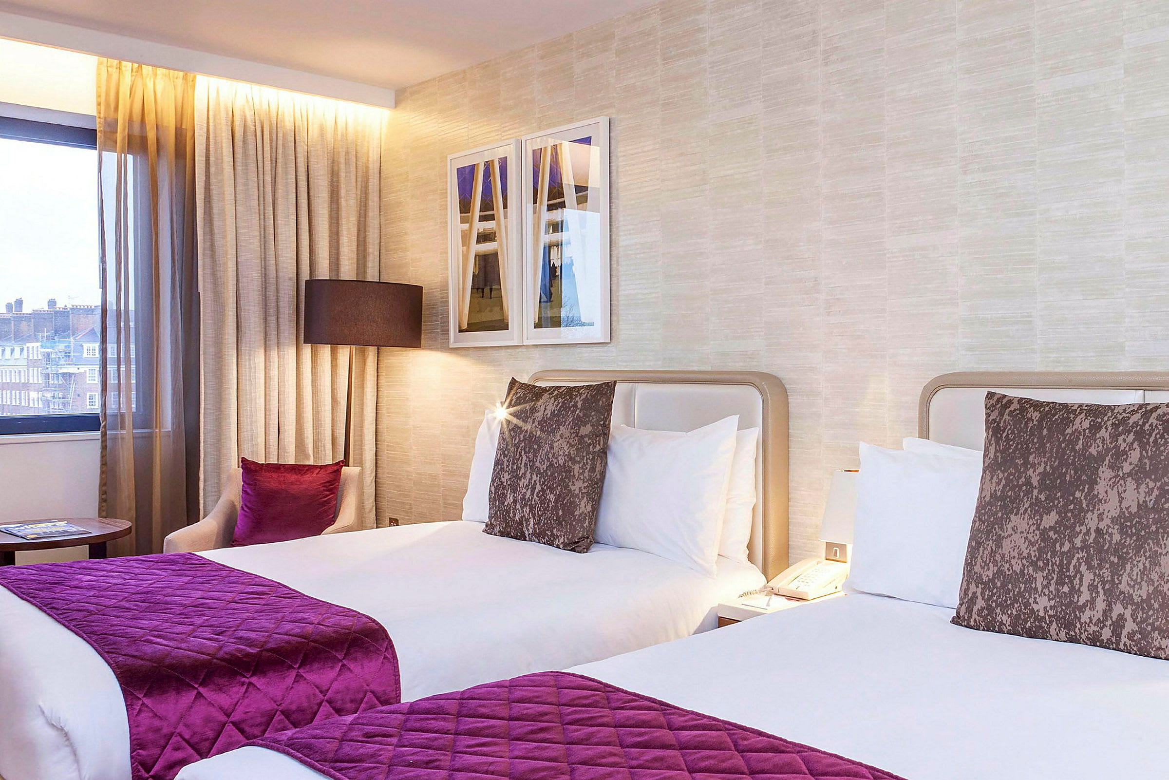 Bild av ett hotellrum med två enkelsängar, dekorativa kuddar och fönster. (AI-genererad text)