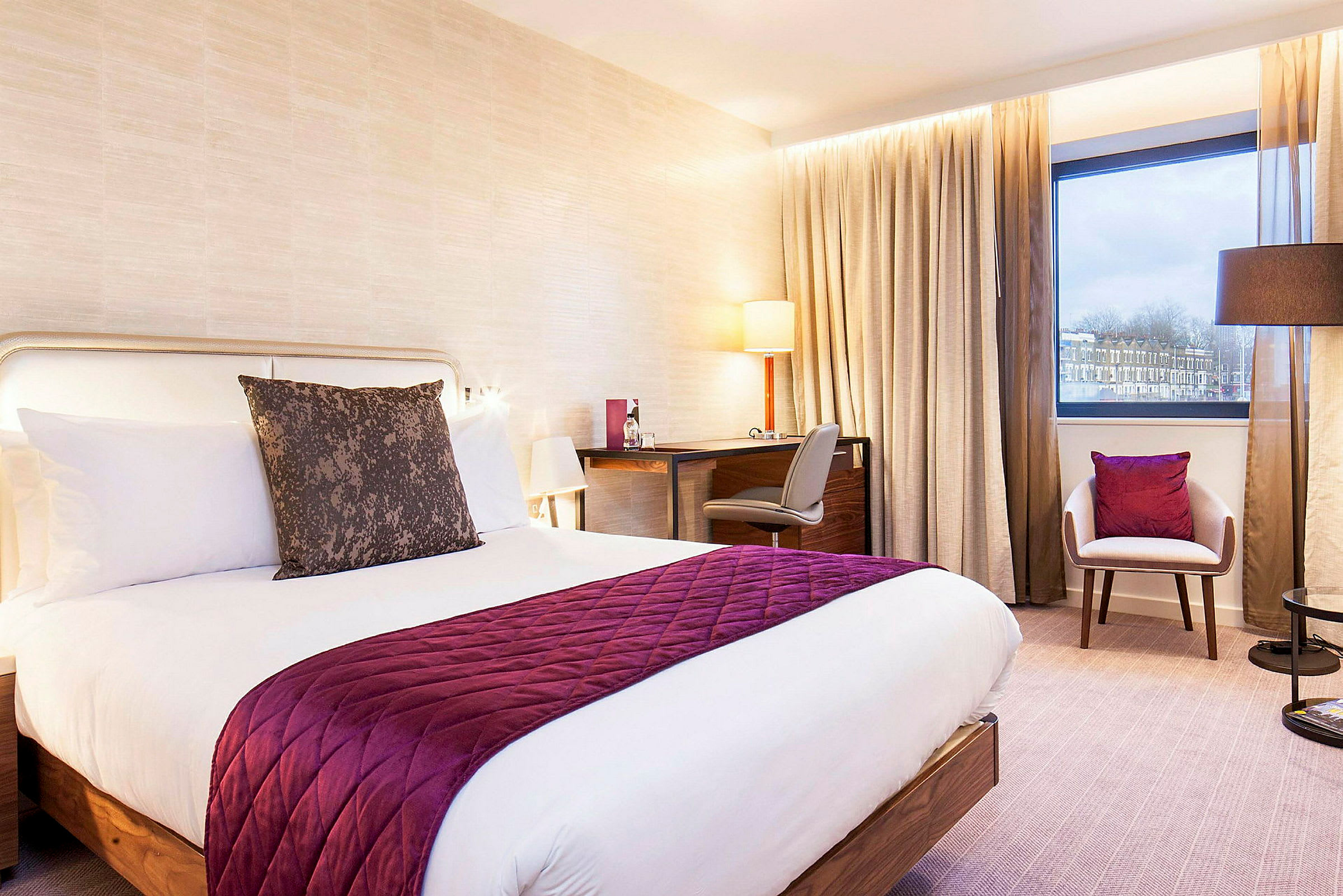 Ett hotellrum med en dubbelsäng, ett skrivbord och en stol, bredvid ett fönster. (AI-genererad text)