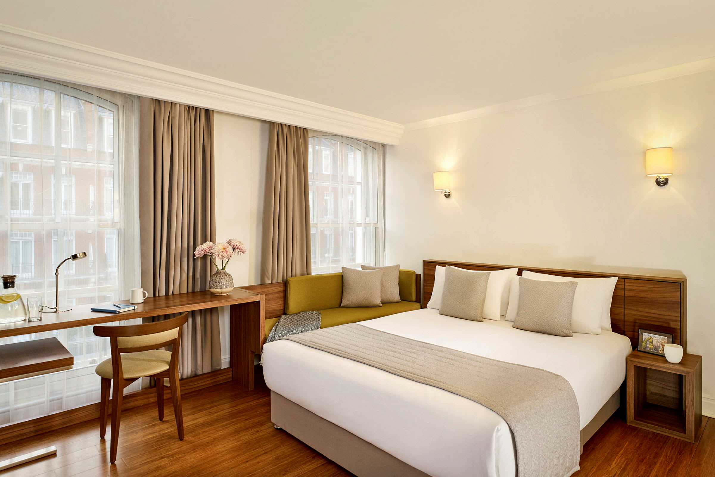 Ett hotellrum med en dubbelsäng, en sittmöbel och ett skrivbord bredvid ett fönster. (AI-genererad text)