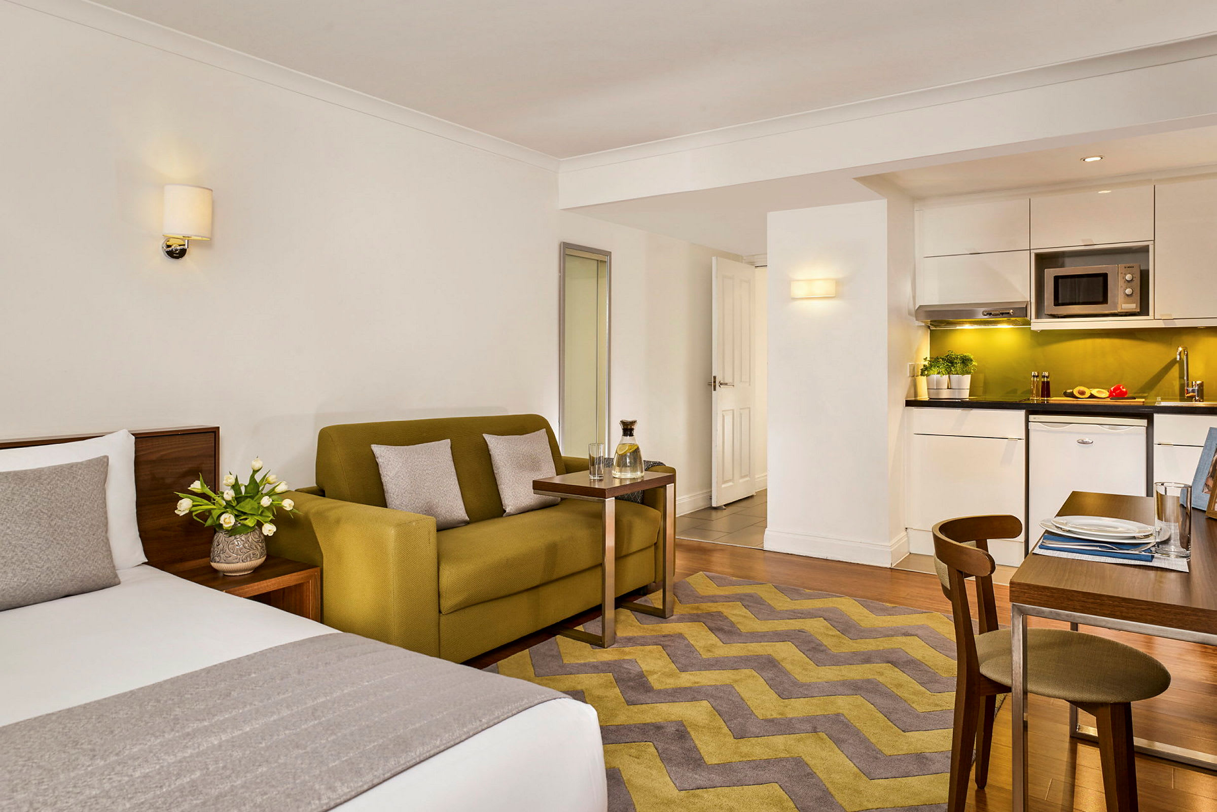 Ett modernt hotellrum med säng, soffa, bord och ett kök med matplats. (AI-genererad text)