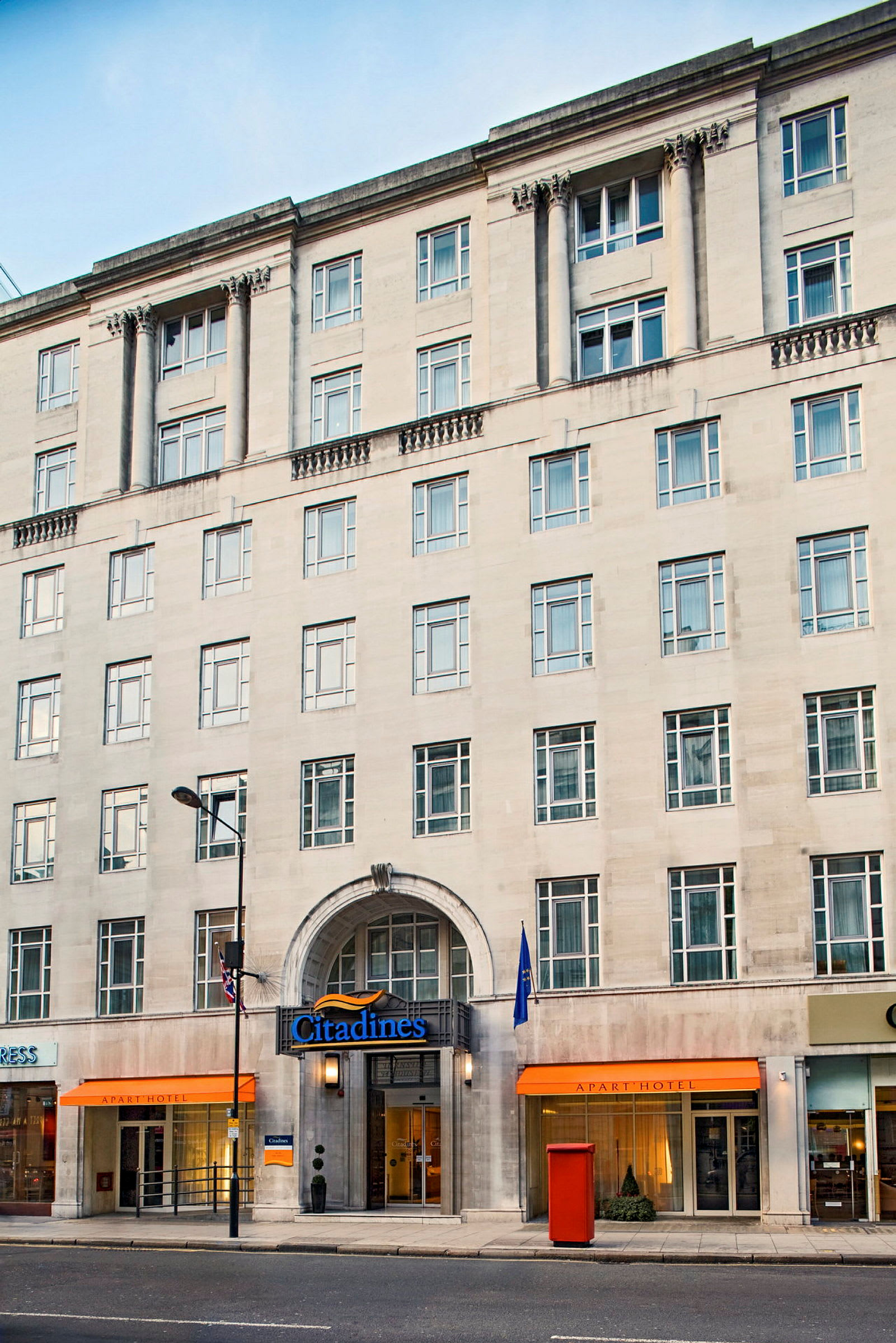 En flerfaldig byggnad med namnet Citadines och ingångar till ett hotell och butiker. (AI-genererad text)