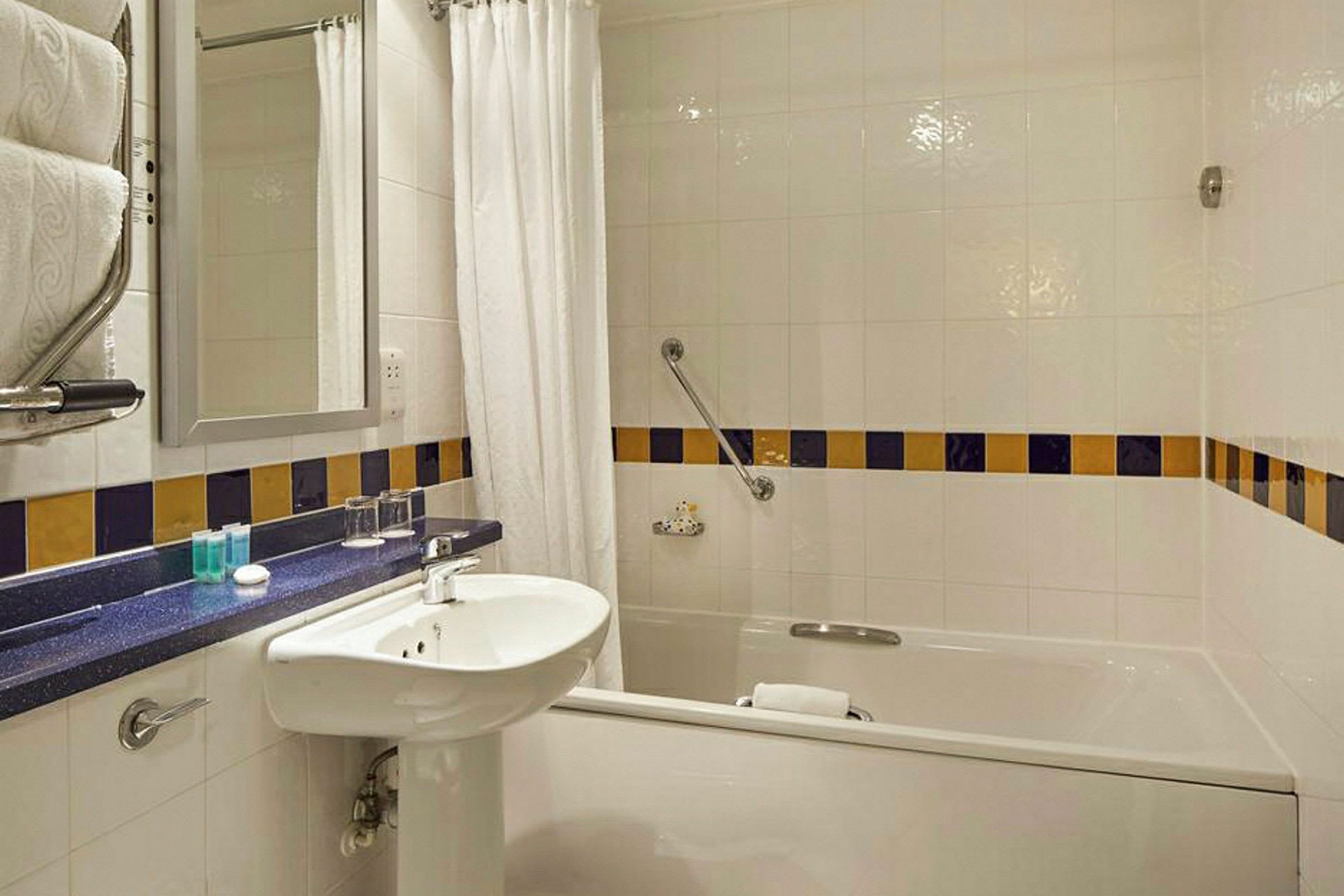Hotellbadrum med badkar, handfat och spegel. (AI-genererad text)