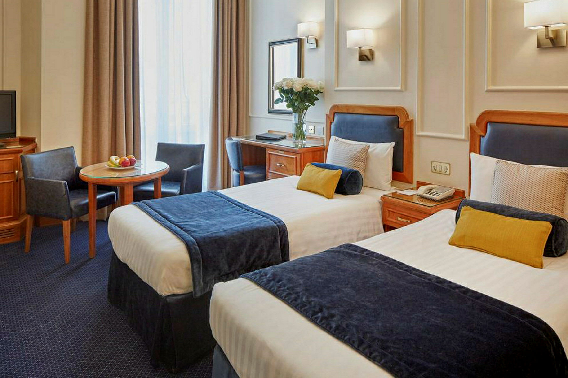 Hotellrum med två enkelsängar, bord och stolar. (AI-genererad text)