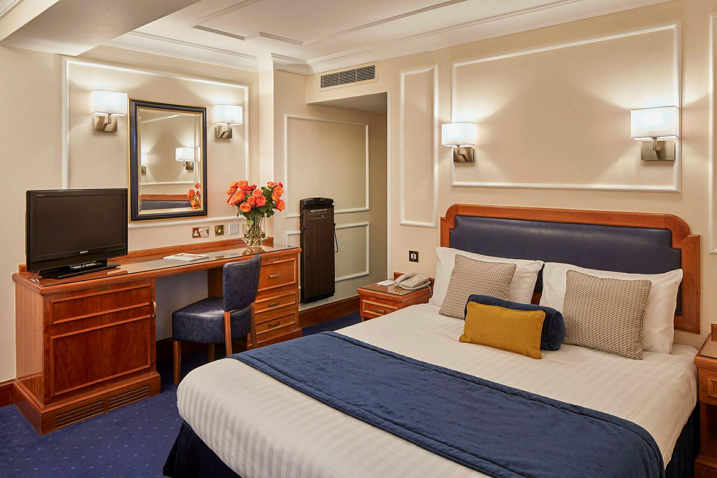 Hotellrum med en säng, skrivbord, stol och spegel. (AI-genererad text)