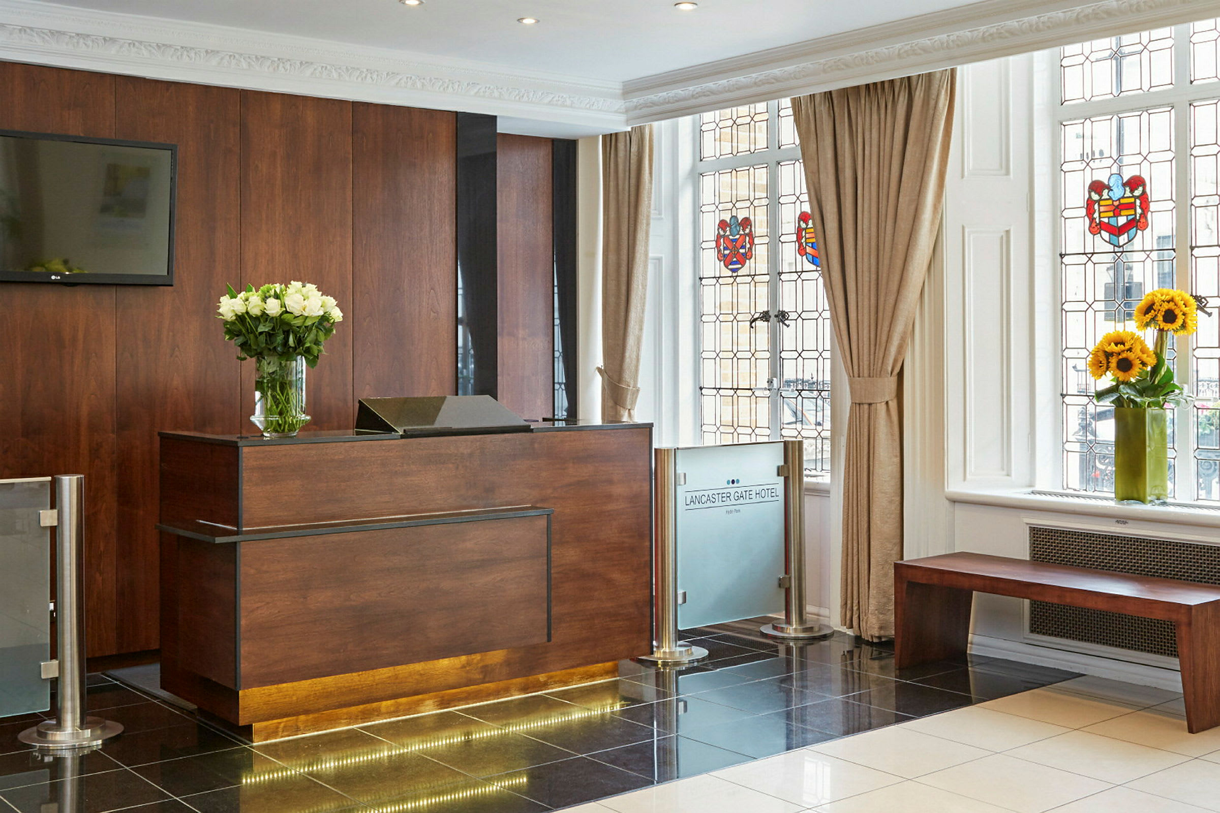 Hotellreception med ett träskrivbord och en vas med vita blommor, bredvid fönster med färgade dekorationer. (AI-genererad text)