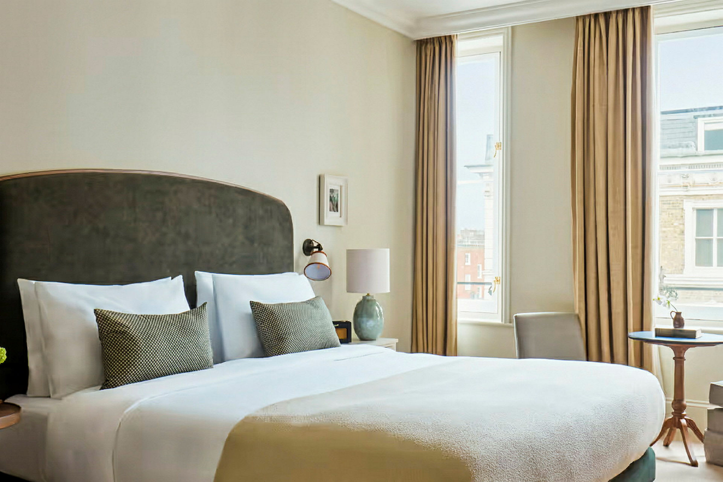 Ett elegant hotellrum med en stor säng, två kuddar, ett nattduksbord och stora fönster med gardiner. (AI-genererad text)