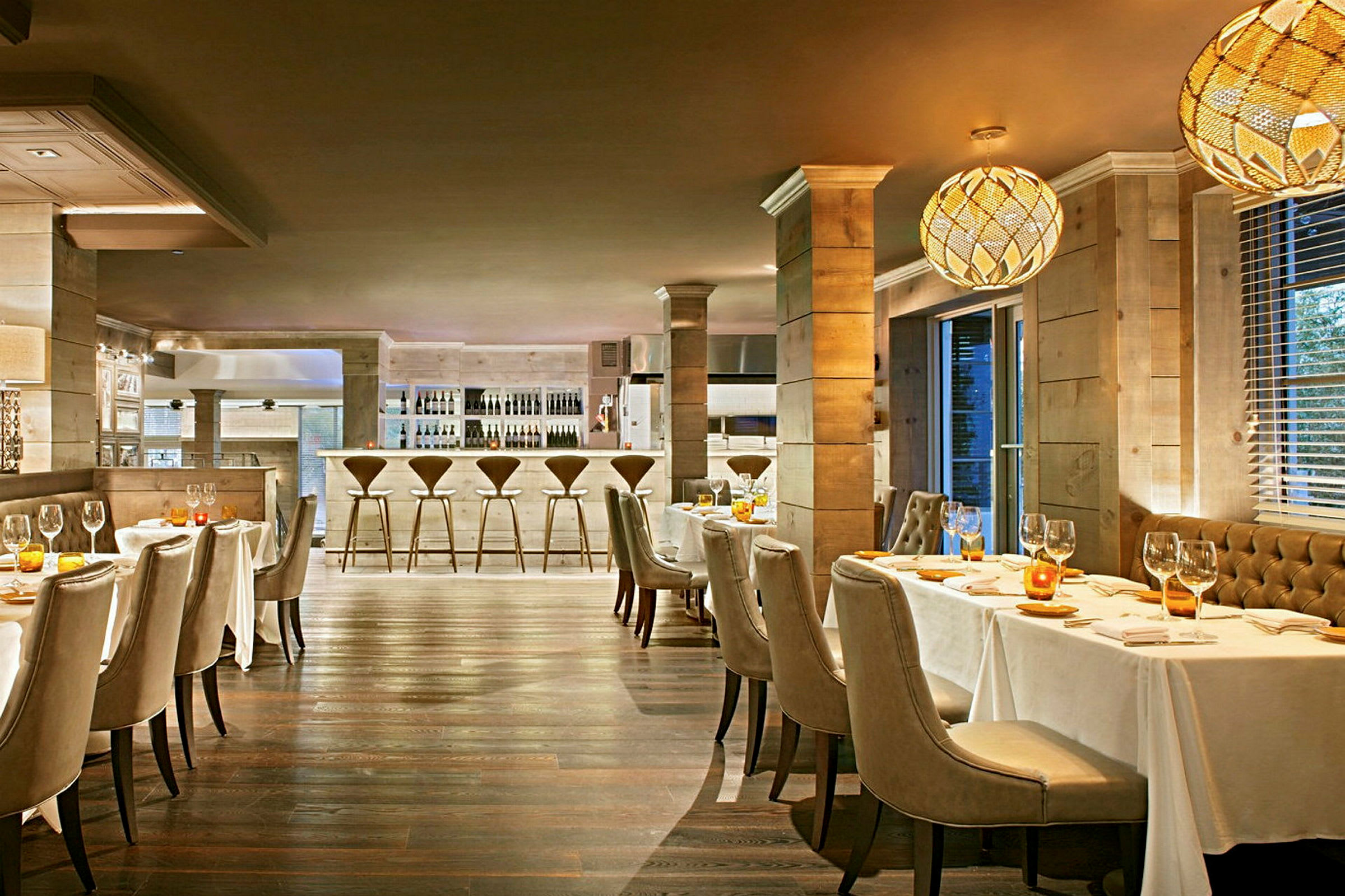 En elegant restaurang med bord täckta med vita dukar, stoppade stolar, och en bardisk i bakgrunden. (AI-genererad text)