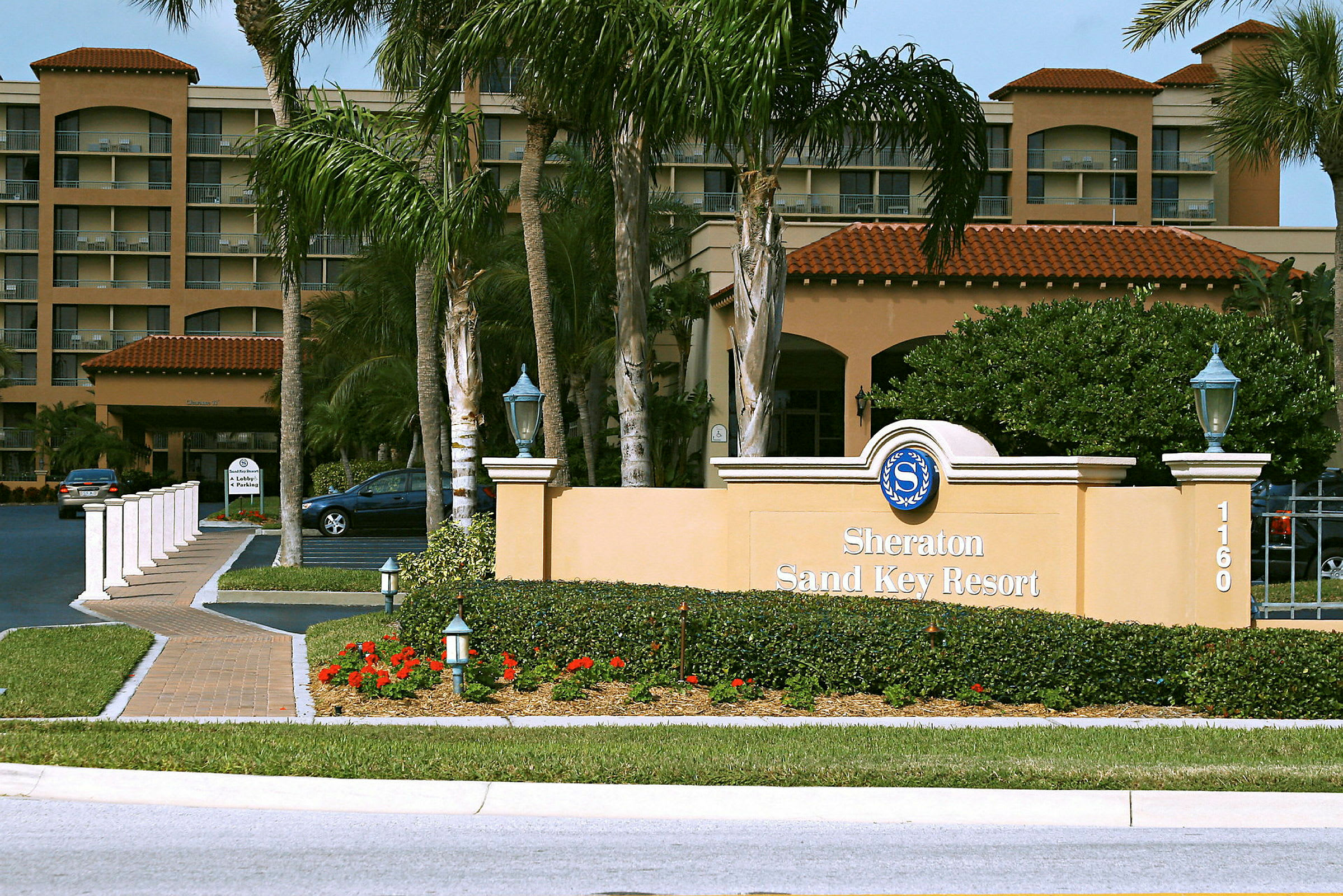 Ett hotell med en skylt som säger "Sheraton Sand Key Resort" omgiven av grönska och palmer. (AI-genererad text)