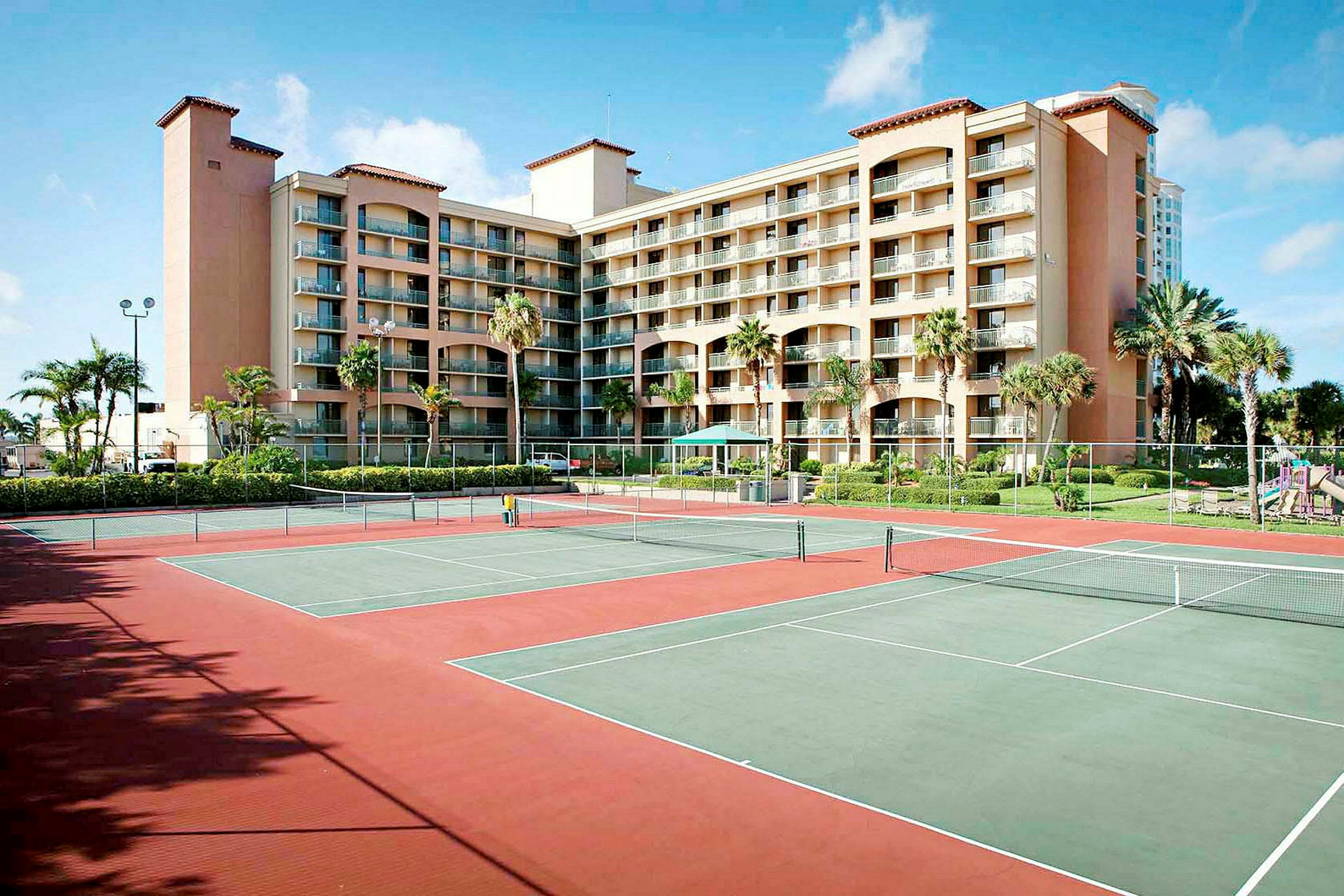 En bild av en byggnad med flera våningar i bakgrunden och två tennisbanor i förgrunden. (AI-genererad text)