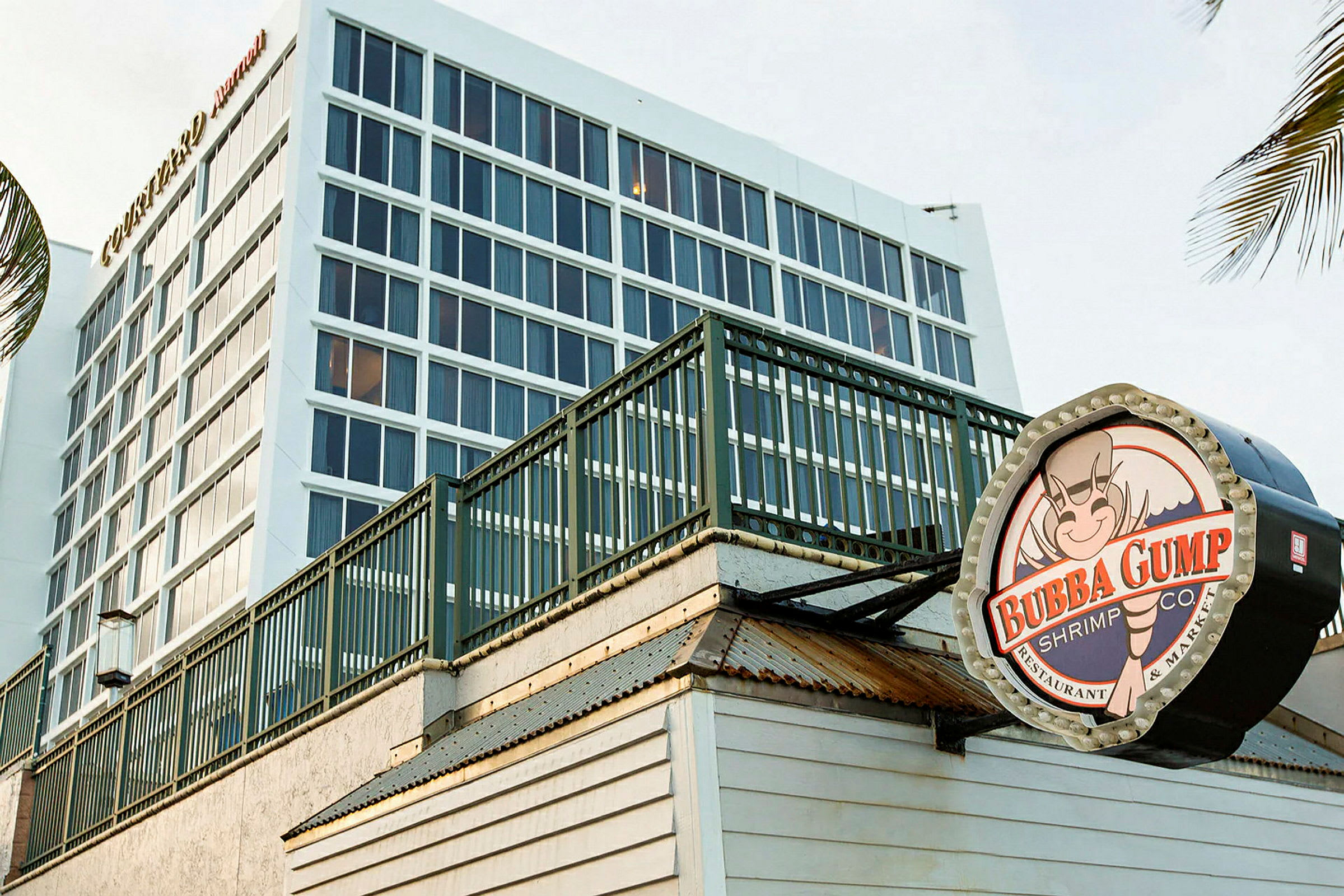 En modern byggnad i bakgrunden med stora fönster, och i förgrunden en skylt för restaurangen Bubba Gump Shrimp Co. (AI-genererad text)