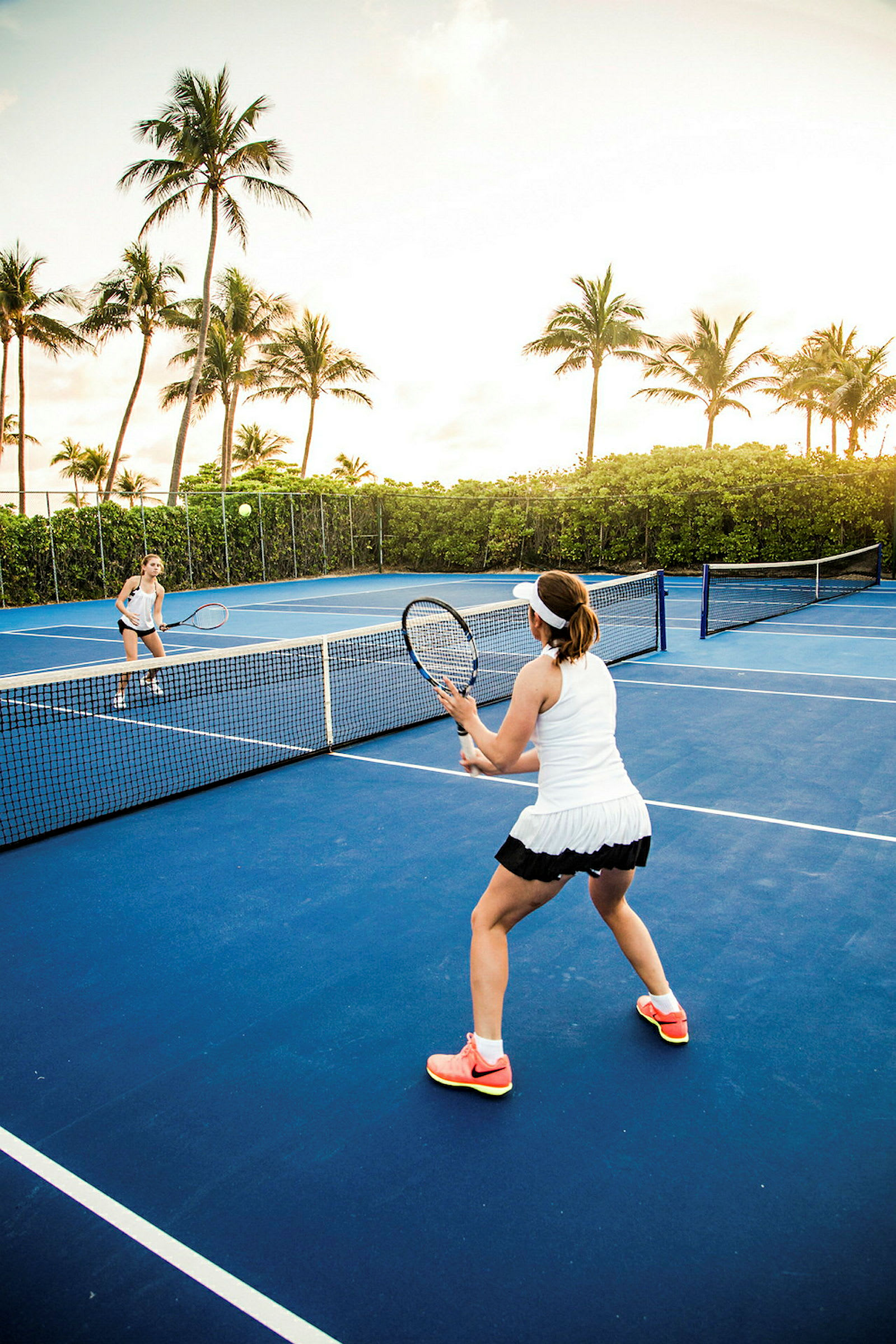 Två personer spelar tennis på en utomhusbana omgiven av palmer. (AI-genererad text)