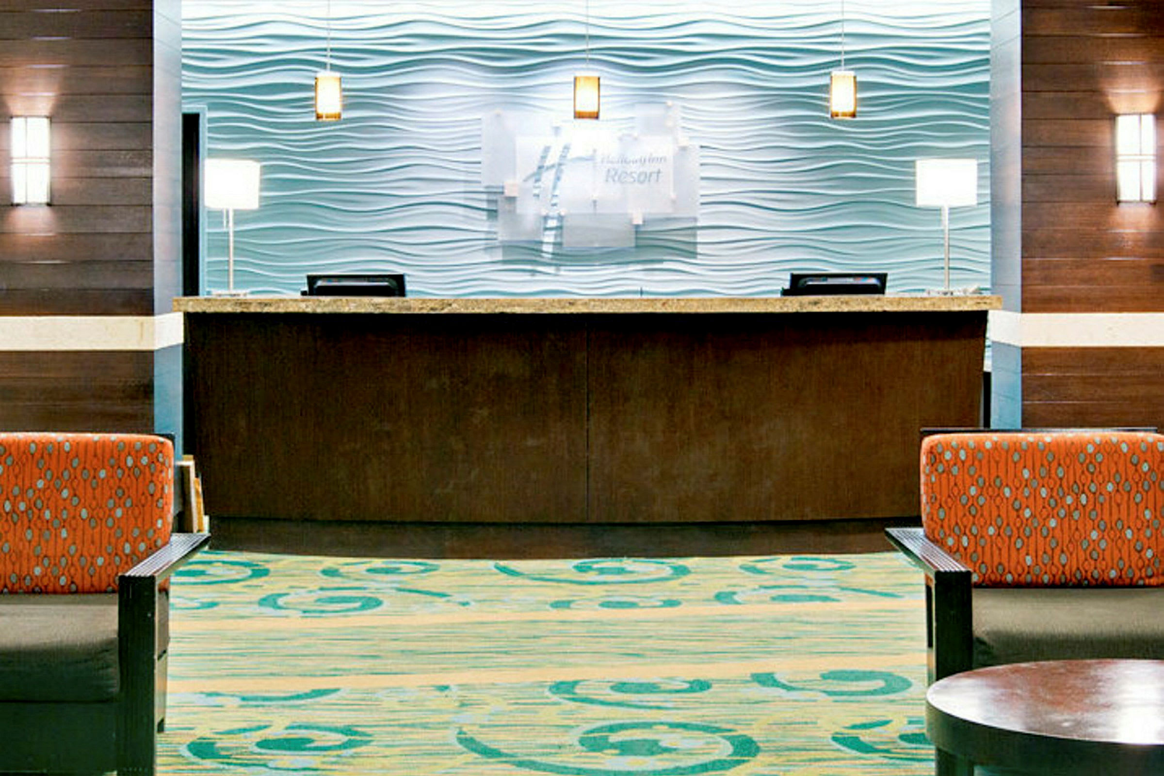 Hotellreception med en disktop av trä och marmorskiva, bakgrund med modern vågformig design. Framför finns sittmöbler med färgglad klädsel. (AI-genererad text)